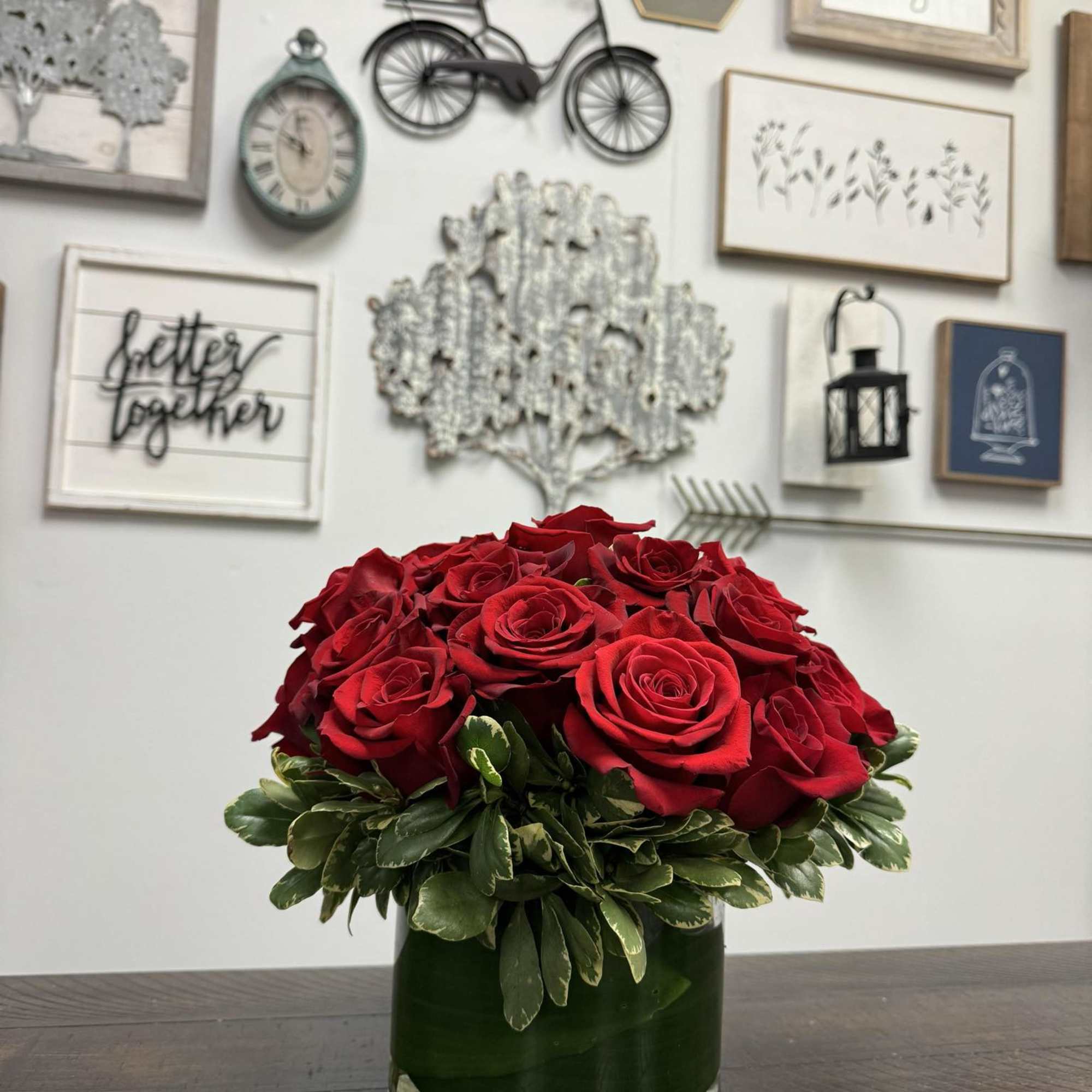 Two dozen red roses in a low, clear vase with greenery.