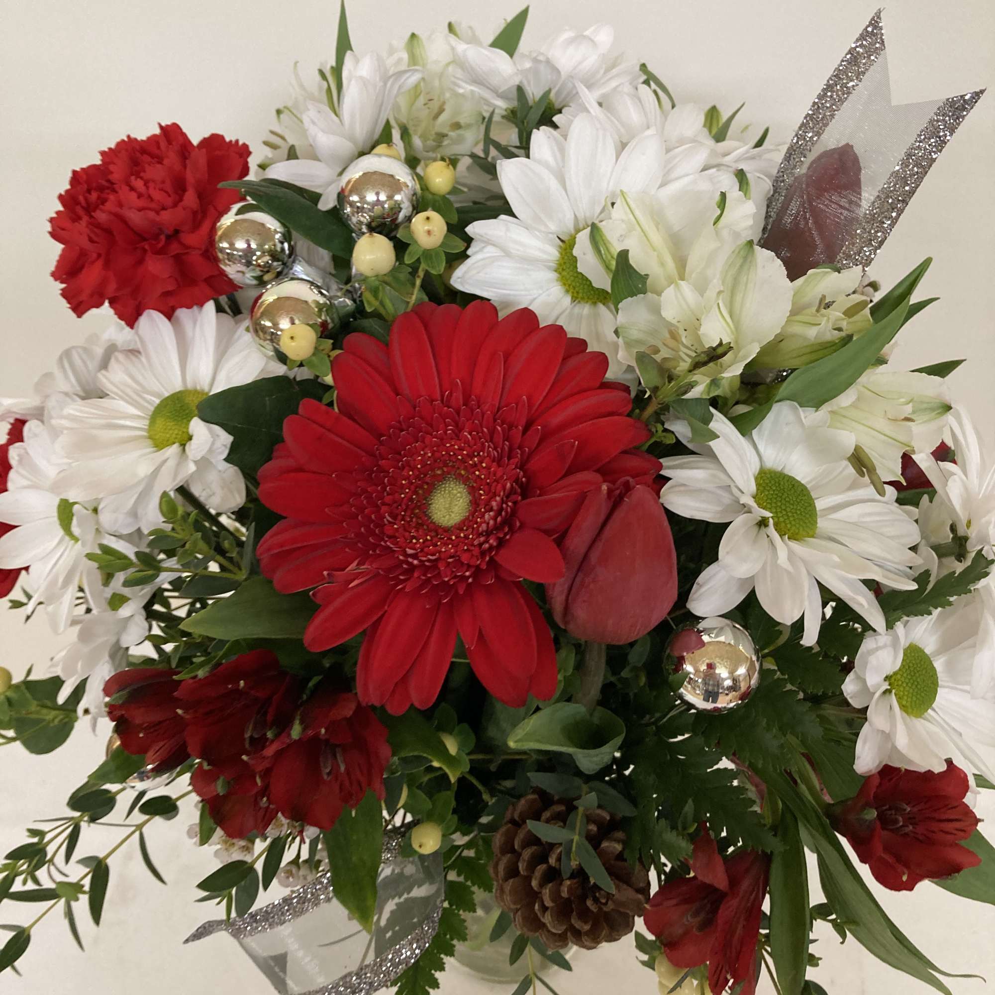 Red and white daisies in a tall glass vase.