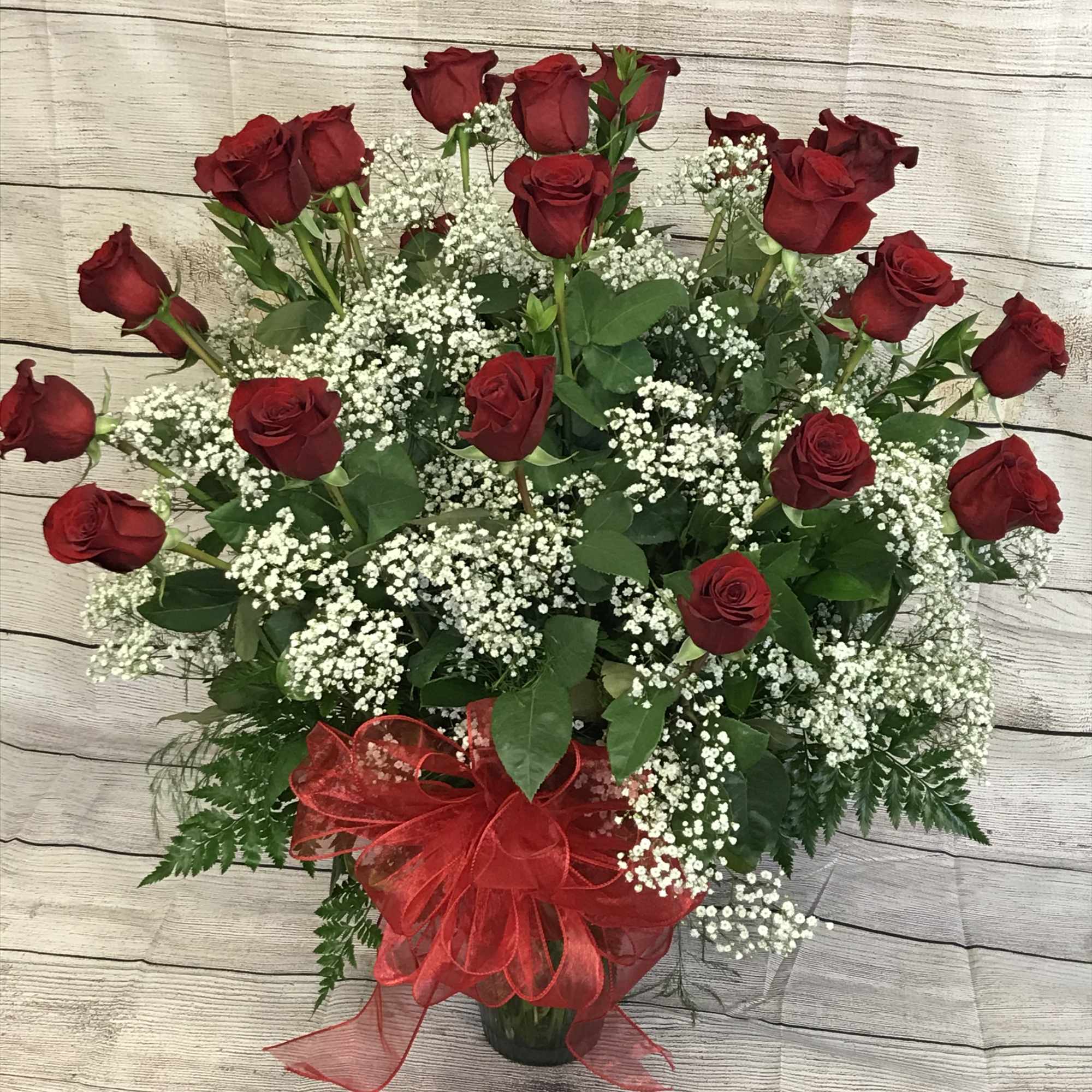 An impressive presentation of two dozen fragrant, long-stemmed red roses accented with