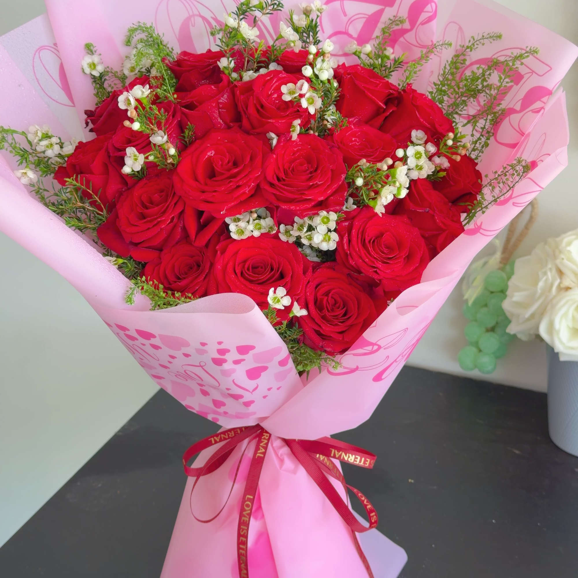 The arrangement includes 19 red roses accented with delicate white blooms and