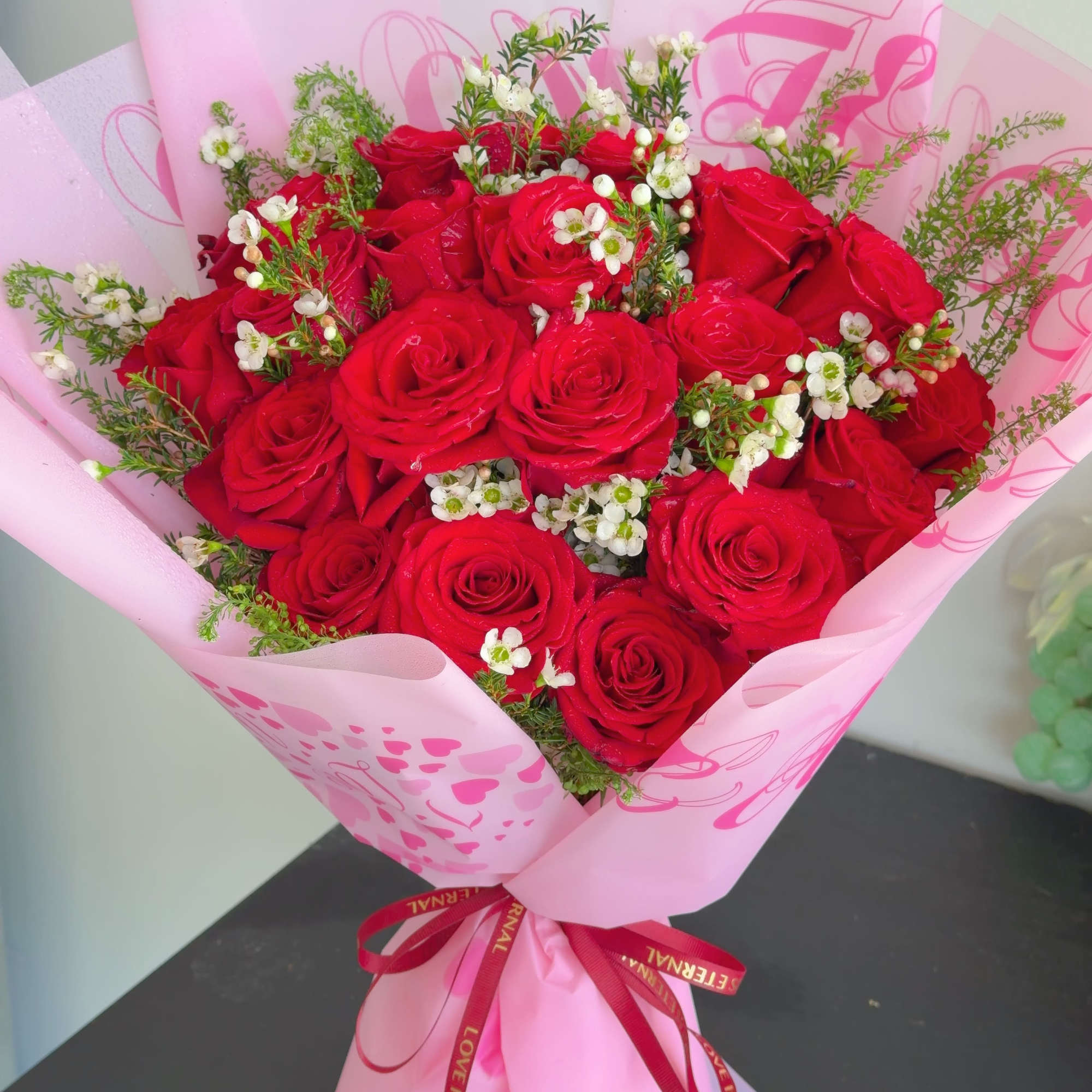The arrangement includes 19 red roses accented with delicate white blooms and