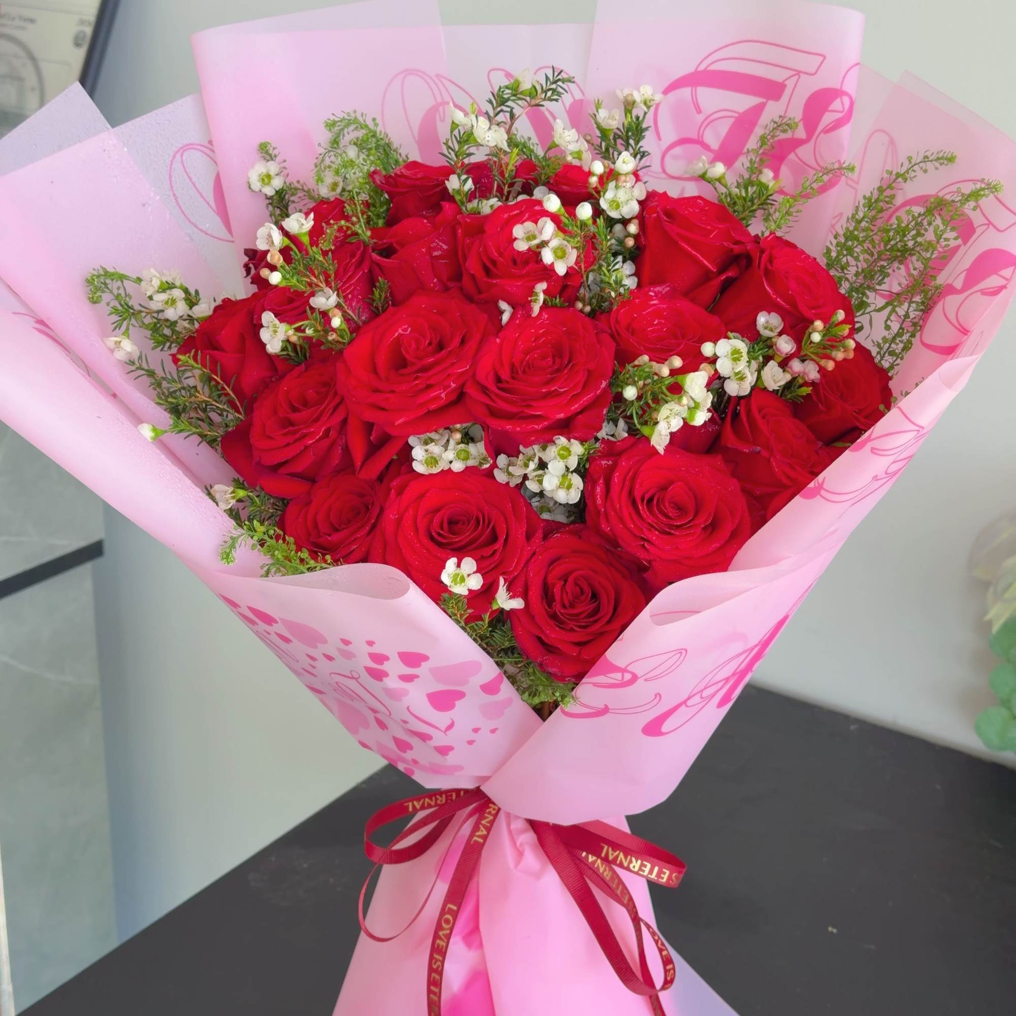 The arrangement includes 19 red roses accented with delicate white blooms and