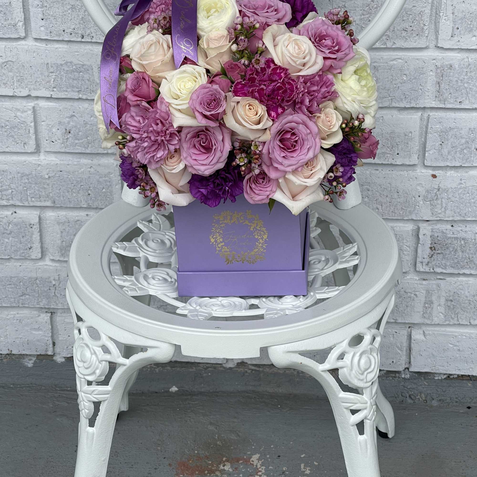 This is a square box filled with lavender roses, wax flower, carnations