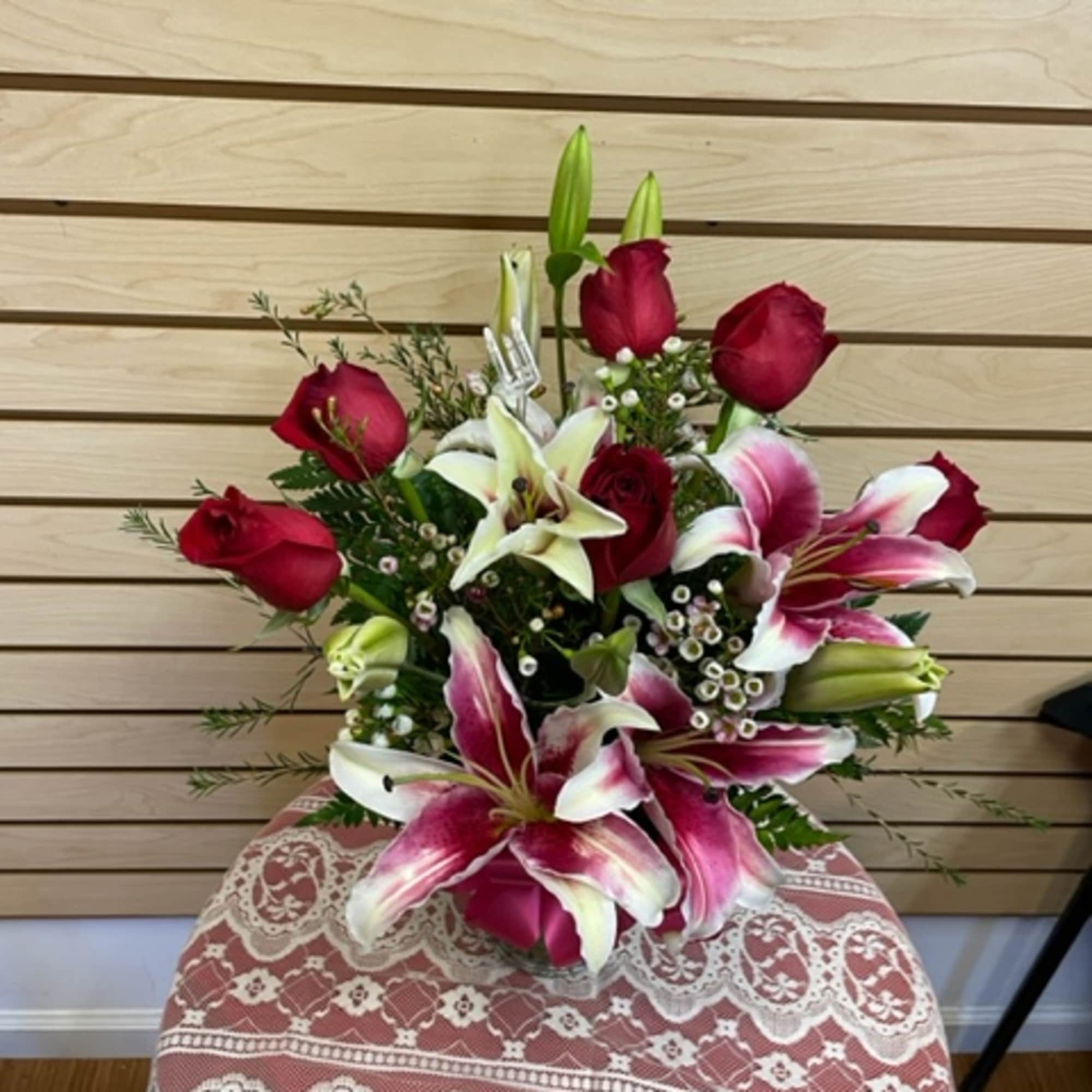 Mixed arrangement with red roses, stargazer lilies, and wax flowers in a
