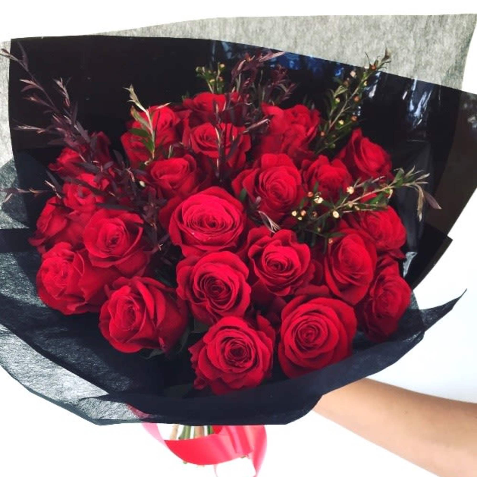 Romantically wrapped red roses with dark burgundy accents in black paper packaging.
