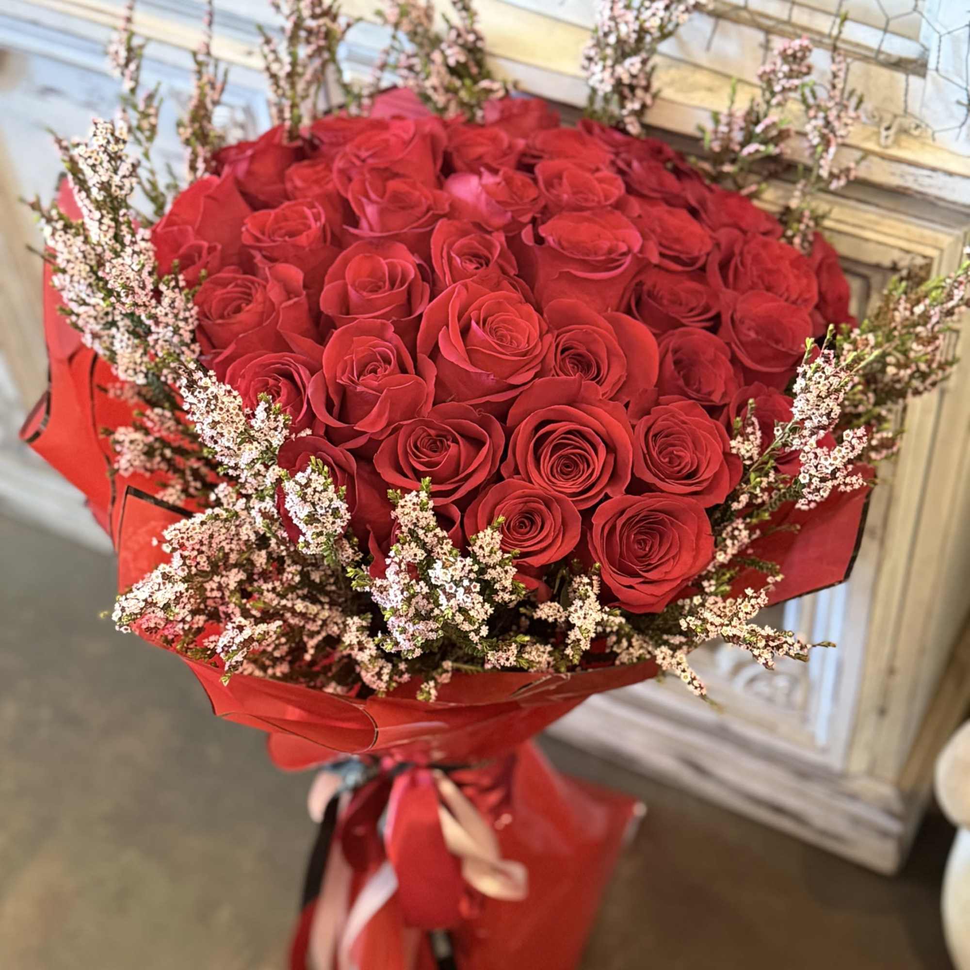 Bold red roses wrapped in deep burgundy paper(variety of colors), accented with