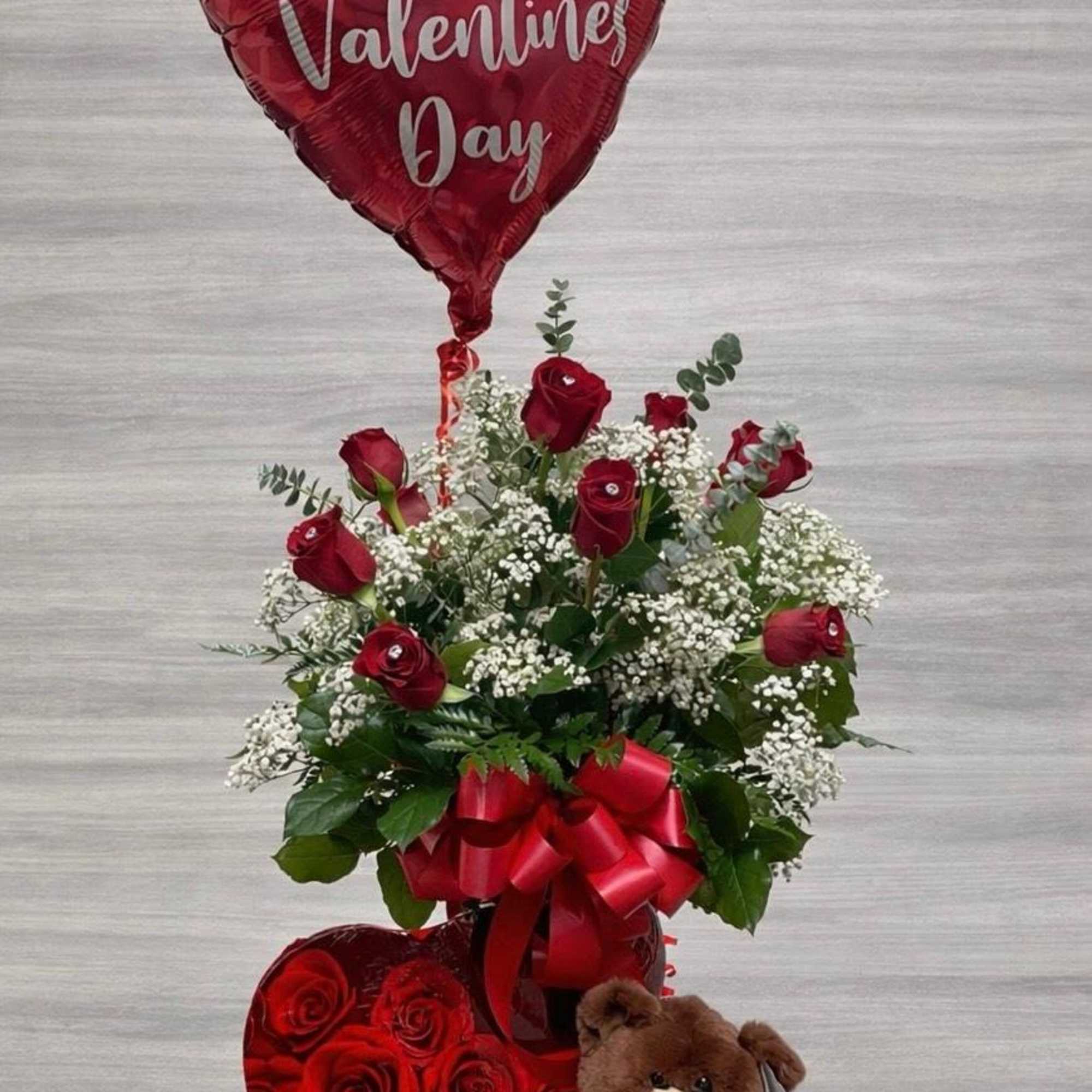 This charming Valentine&rsquo;s arrangement showcases vibrant red roses with faux diamonds, 