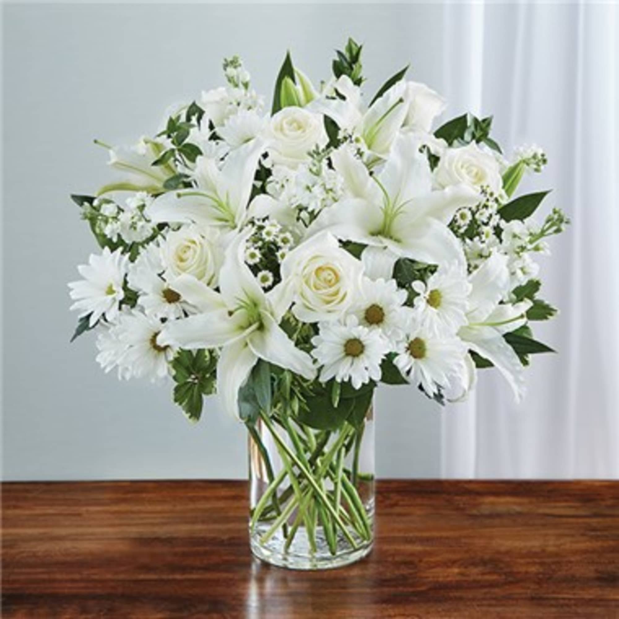 Express your sincere condolences with our elegant all-white arrangement of roses, lilies