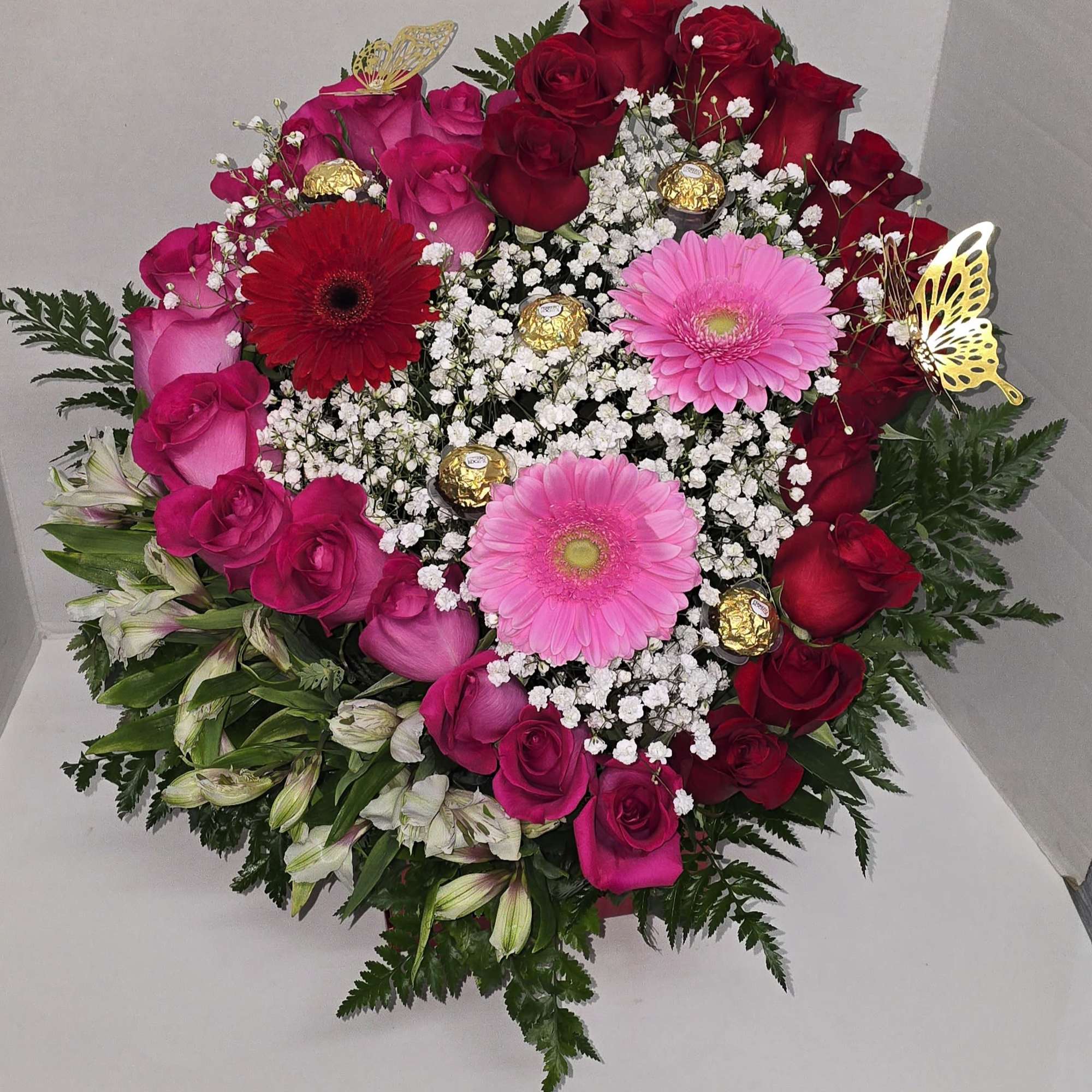 This is a heart-shaped arrangement combining roses, gerberas, and alstroemeria, with chocolates