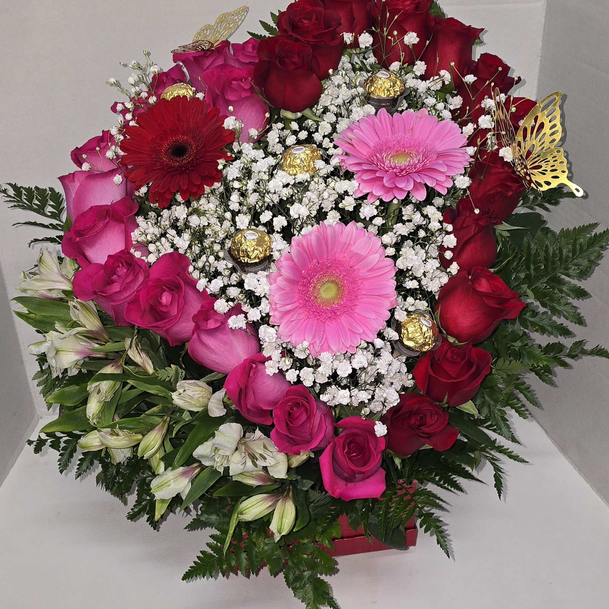 This is a heart-shaped arrangement combining roses, gerberas, and alstroemeria, with chocolates