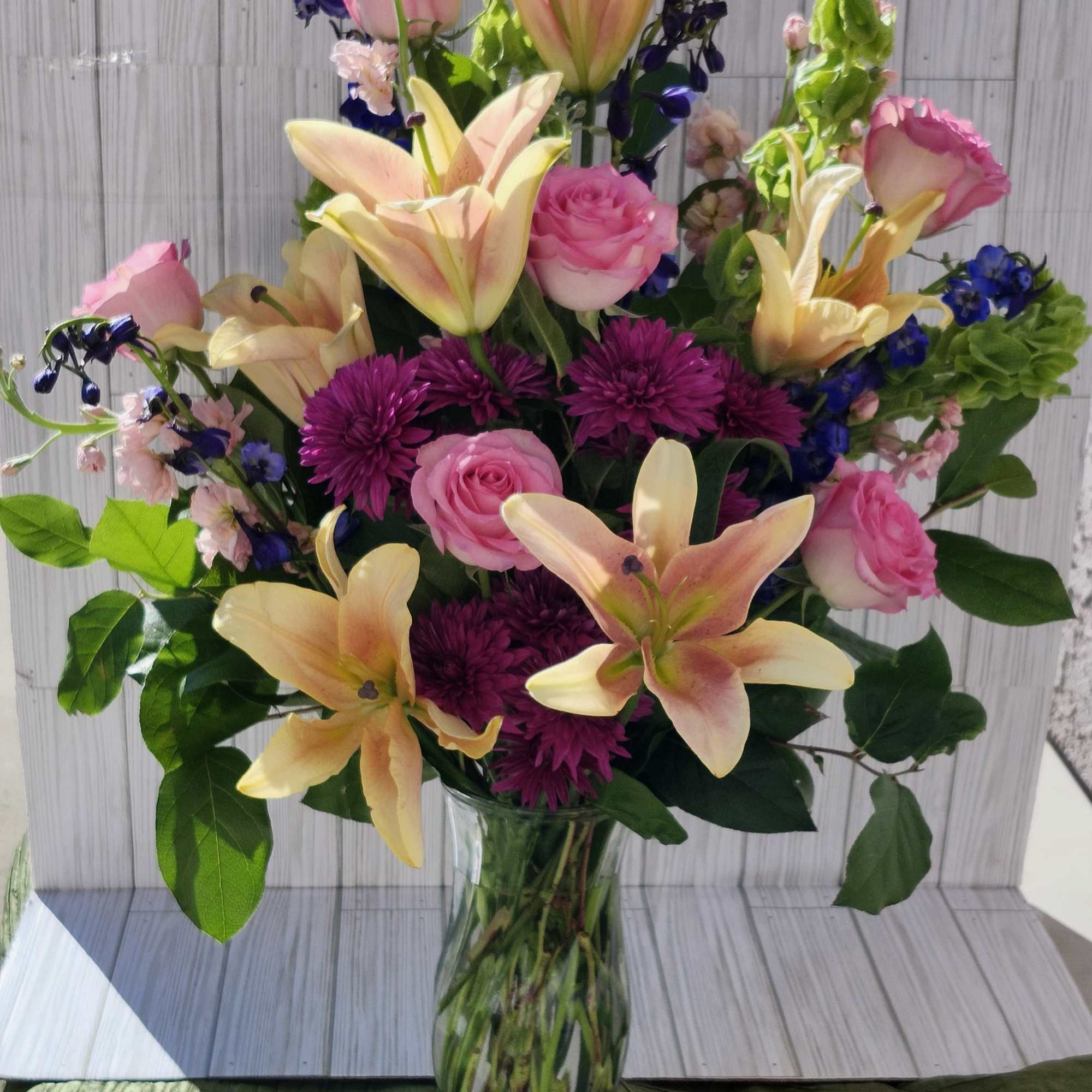 This arrangement contains stargazer lilies, bells of ireland, stock, blue iris, roses