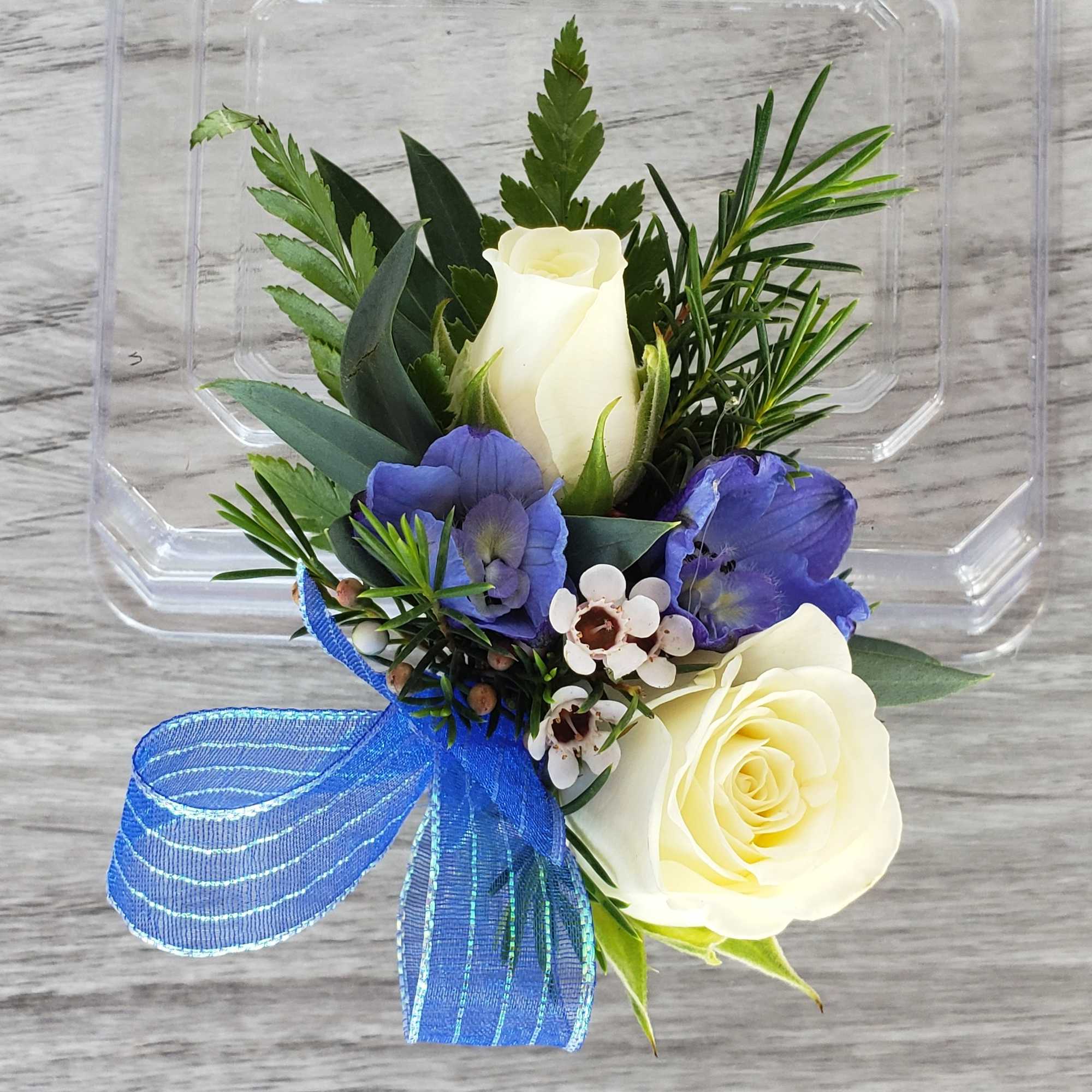 This Boutonniere features white spray roses, and delphinium with accent flowers and