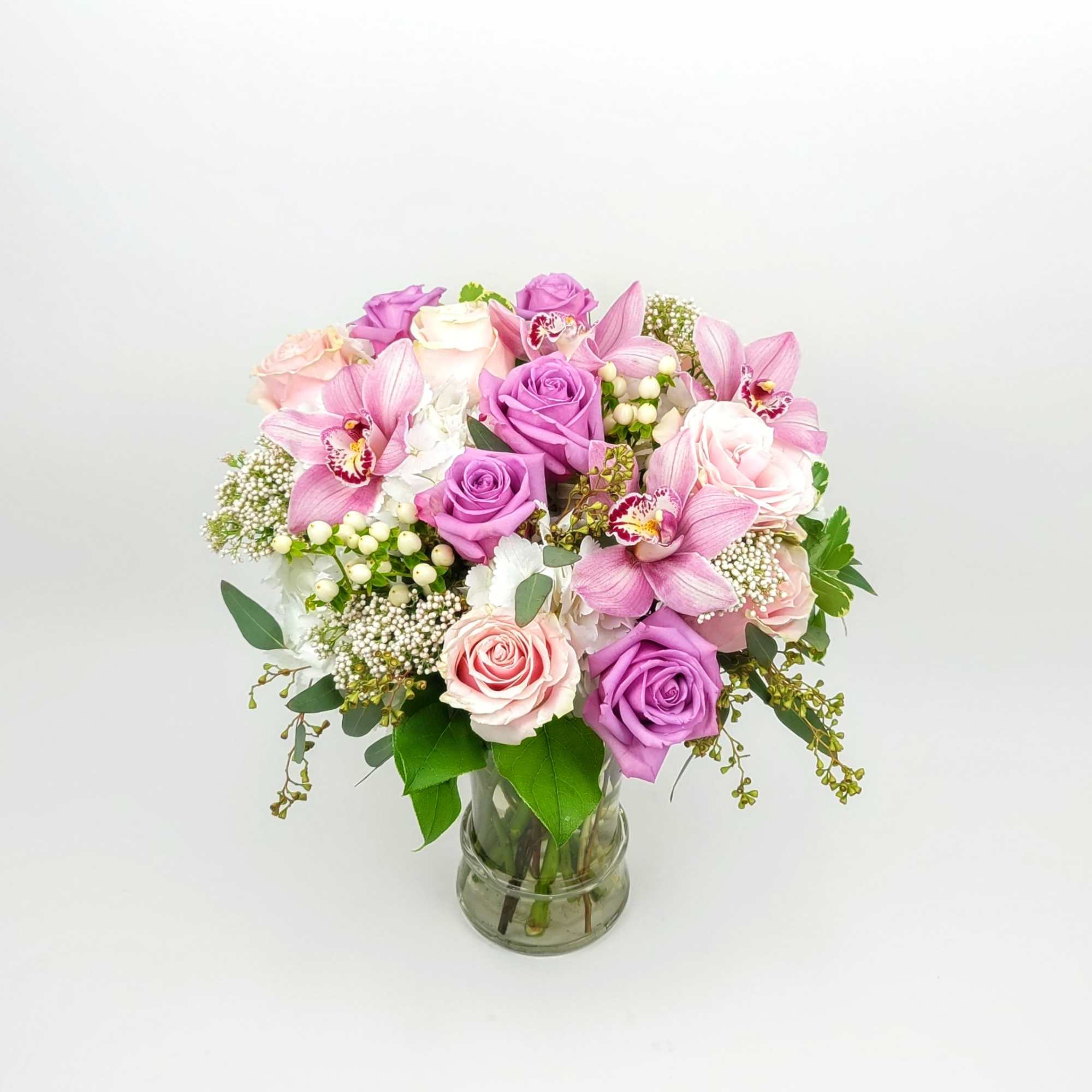 In a clear vase an arrangement with roses, hydrangeas,  cymbidium orchids