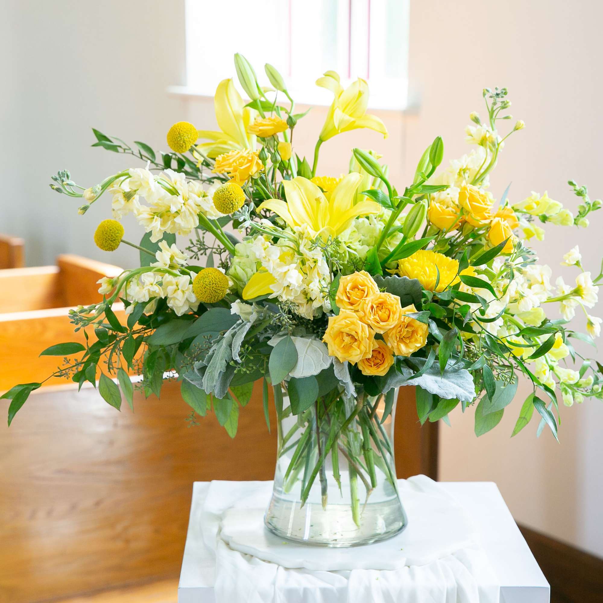 This graceful arrangement of yellow lilies, roses, and soft white blooms offers