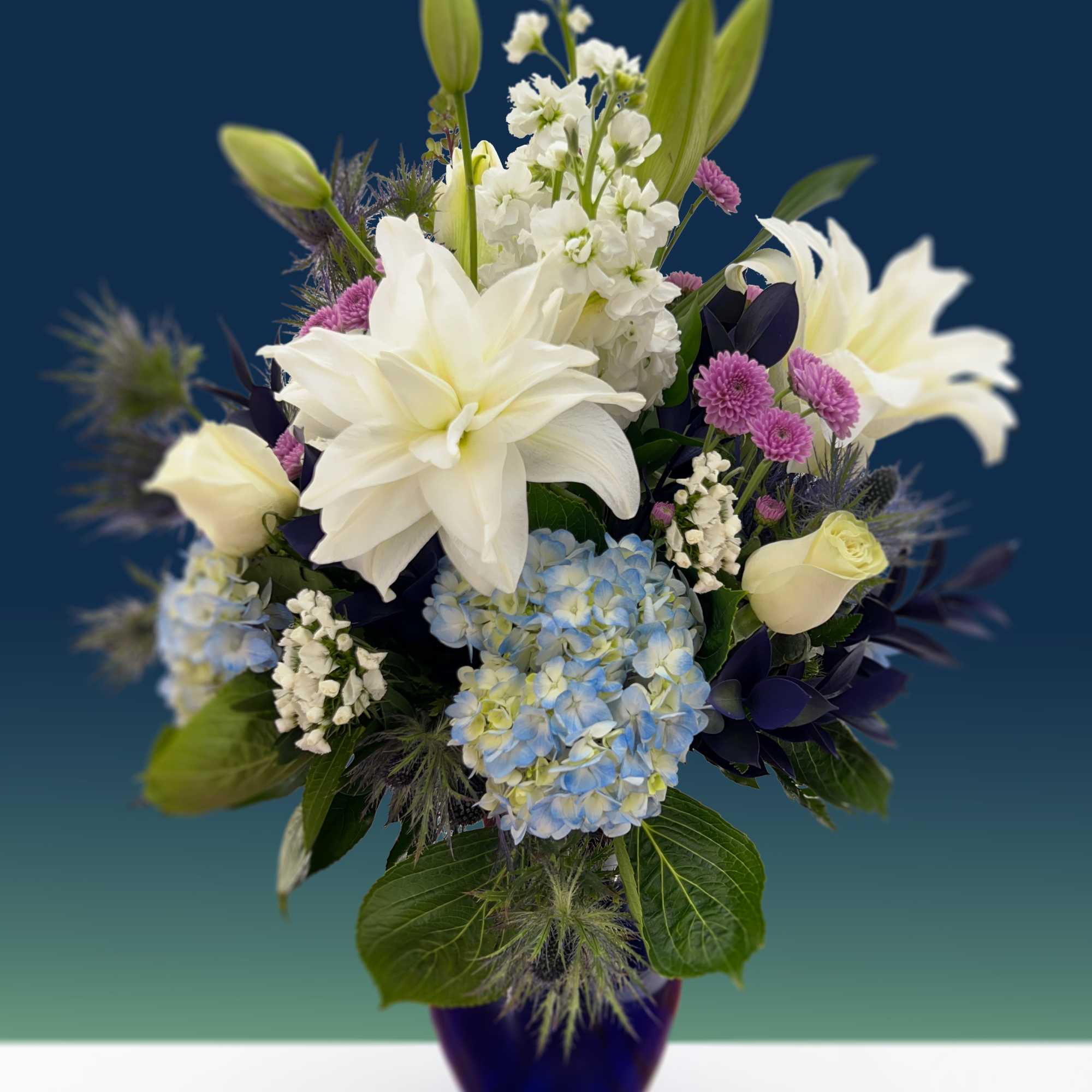 This arrangement is composed of blue thistle, blue hydrangeas, white lilies, white