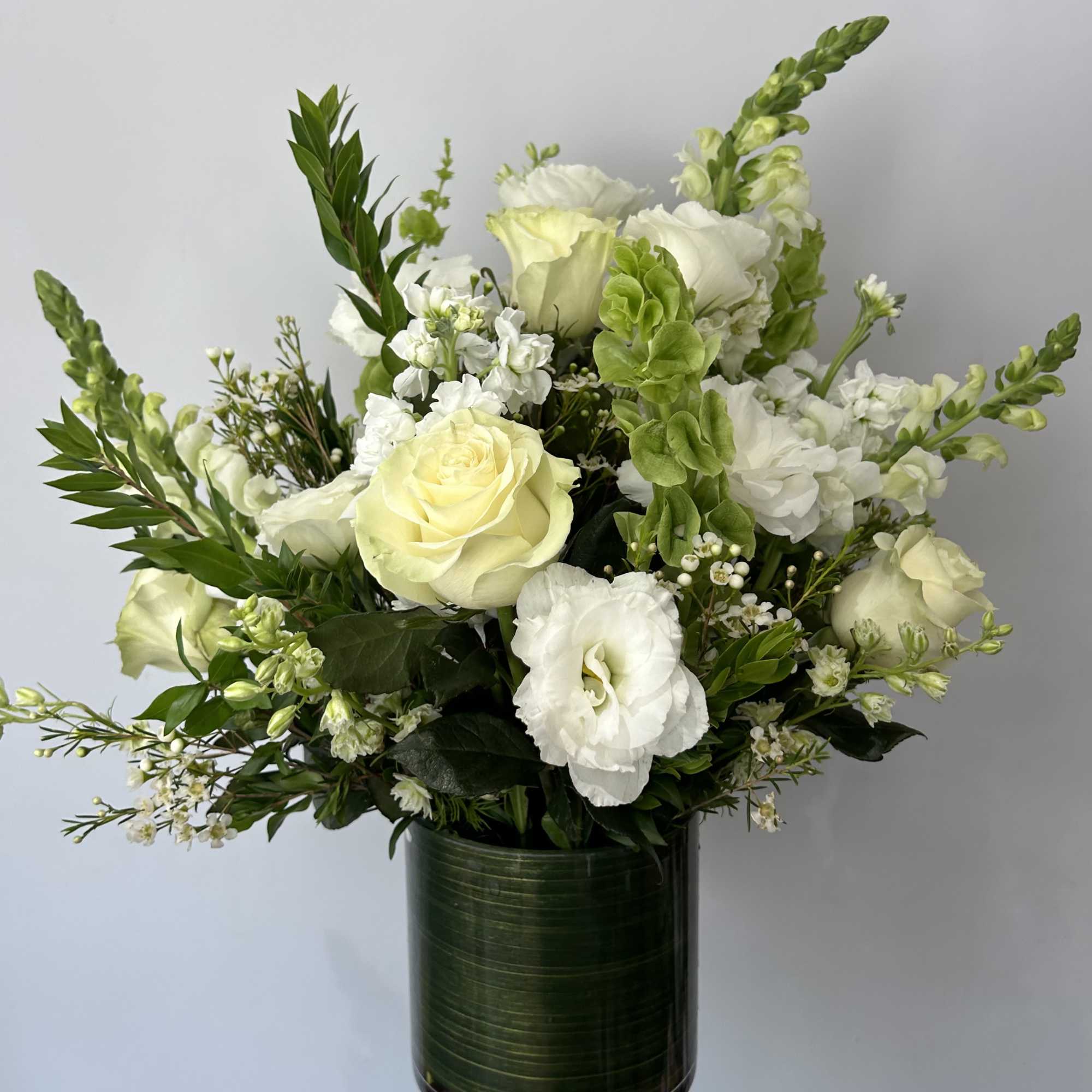 Seasonal white flowers arranged with fillers and greens in a vase.