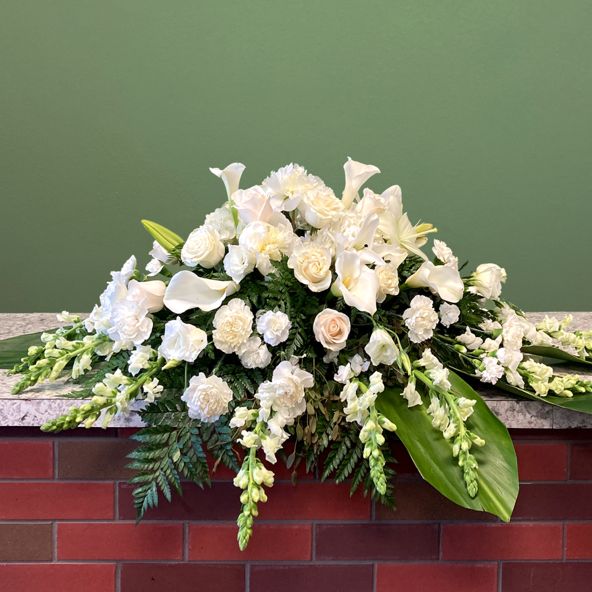 A serene casket spray of flowers, showcasing an all-white palette. Featuring peonies