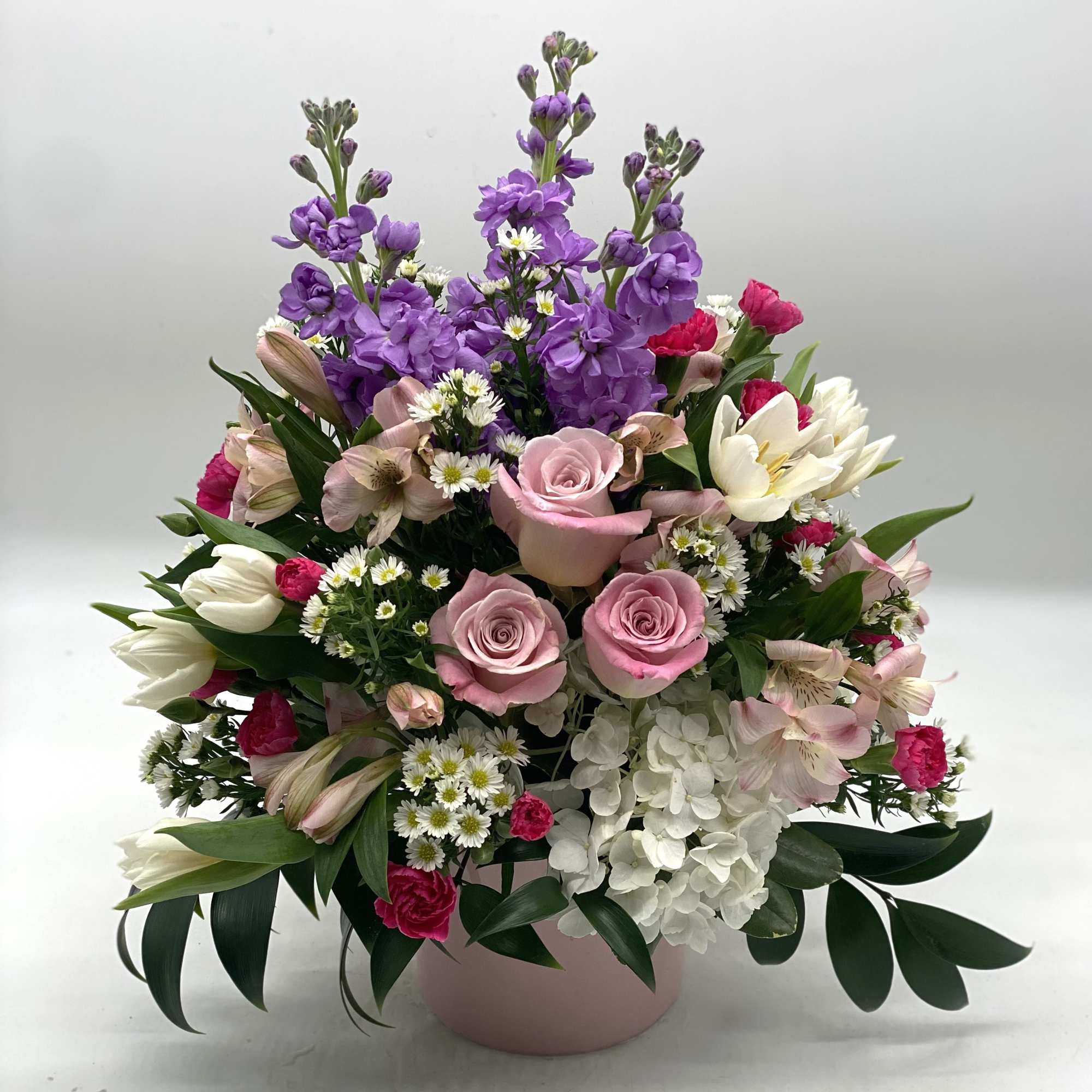 A lush mix of flowers designed in a light pink ceramic container.