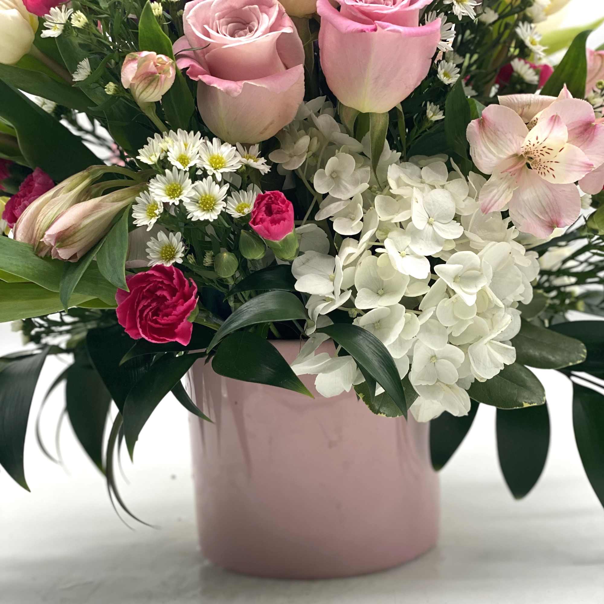 A lush mix of flowers designed in a light pink ceramic container.