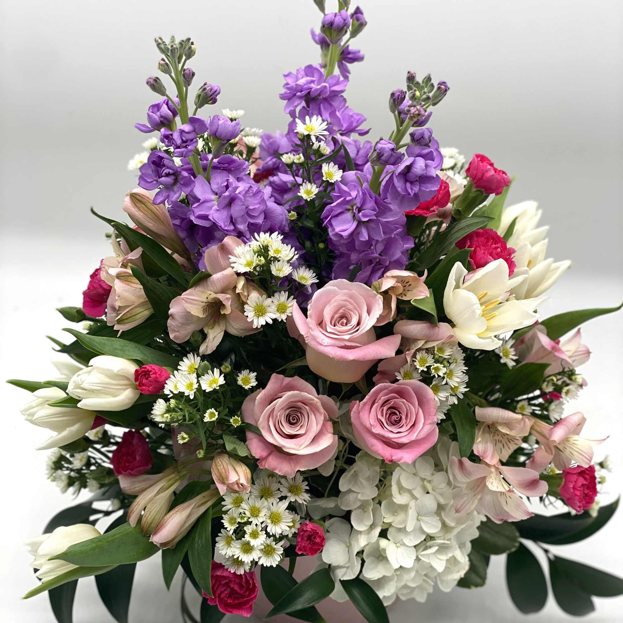 A lush mix of flowers designed in a light pink ceramic container.