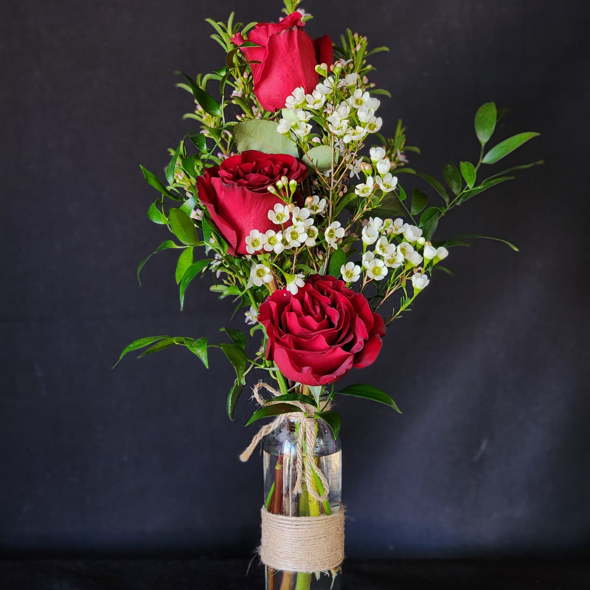 3 red roses in a bud vase with the citrus fragrance of