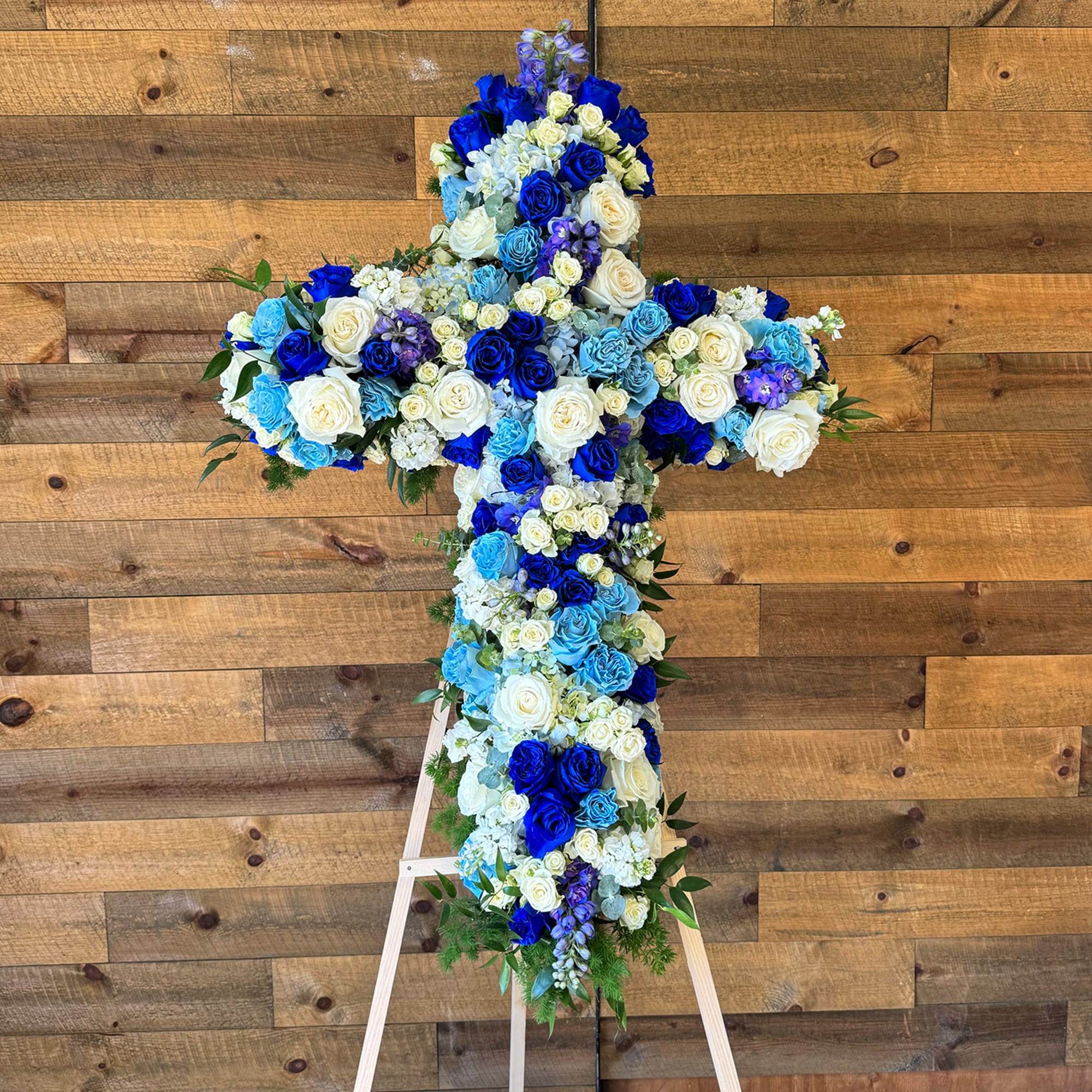 Blue flowers, light blue flowers, white flowers, and greenery. The standing cross