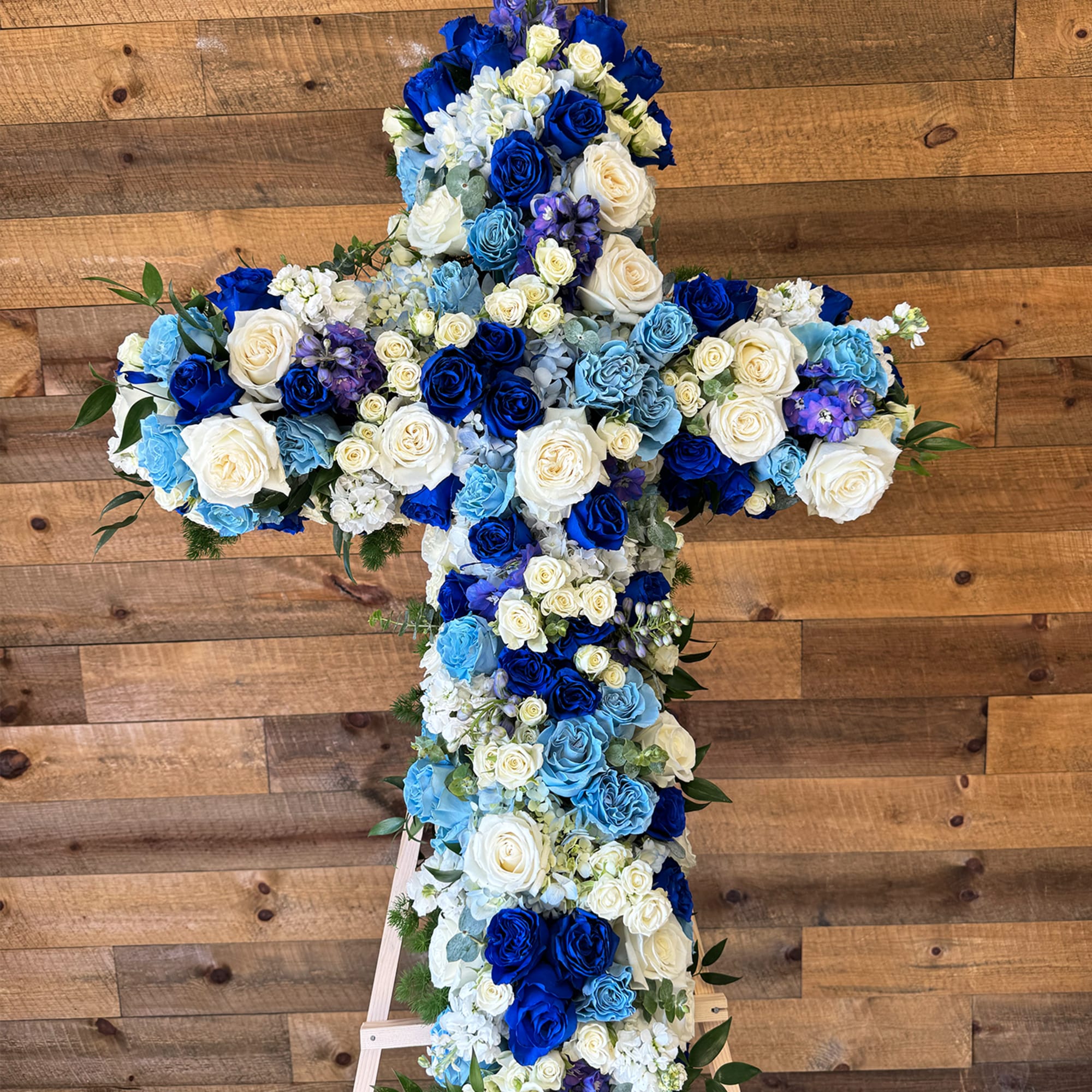 Blue flowers, light blue flowers, white flowers, and greenery. The standing cross