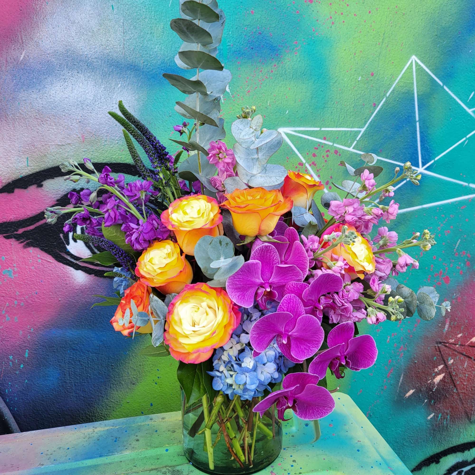 An arrangement made in a tall glass cylinder with Roses, hydrangeas, orchids