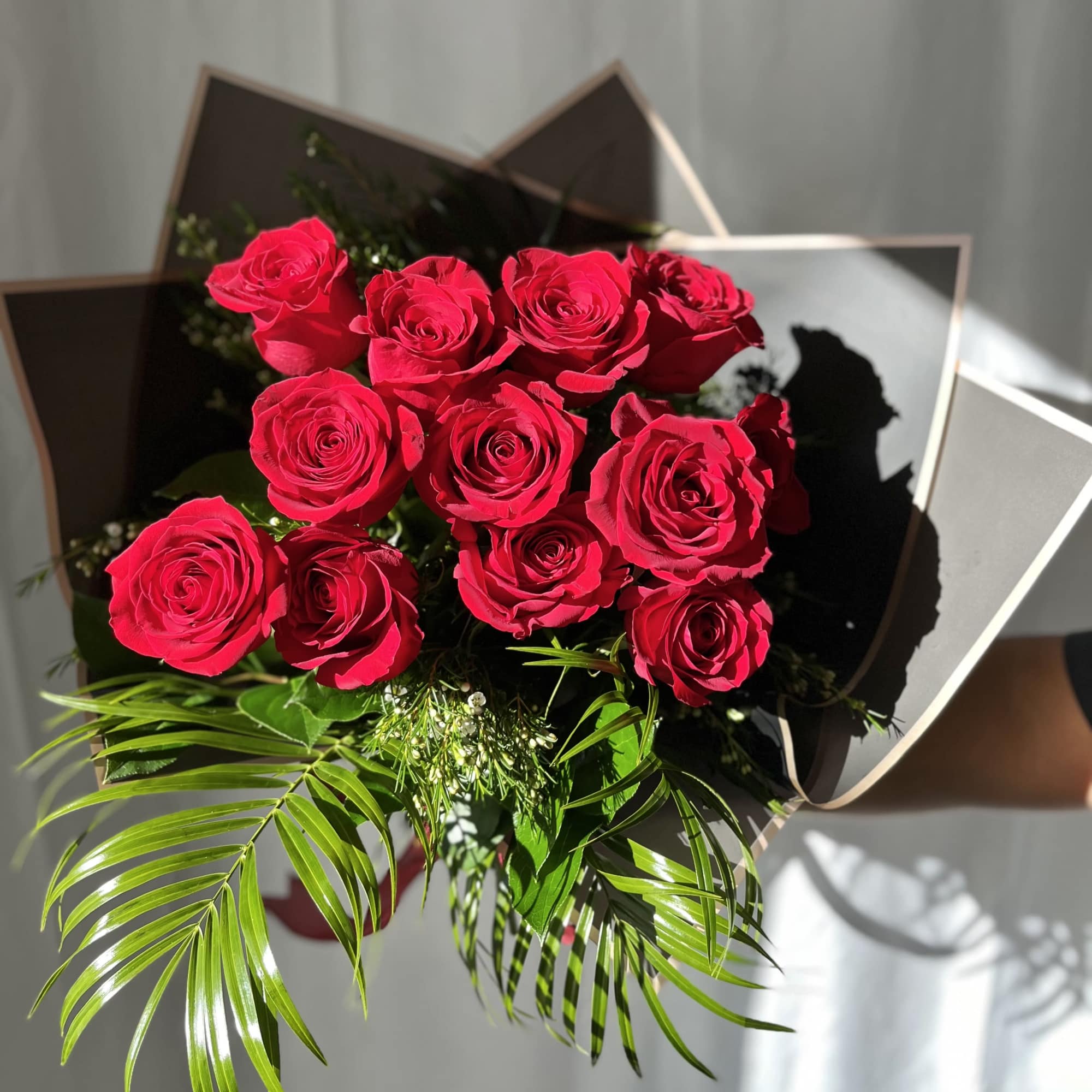 Featuring luxurious red roses arranged in lush greenery, wrapped in premium paper