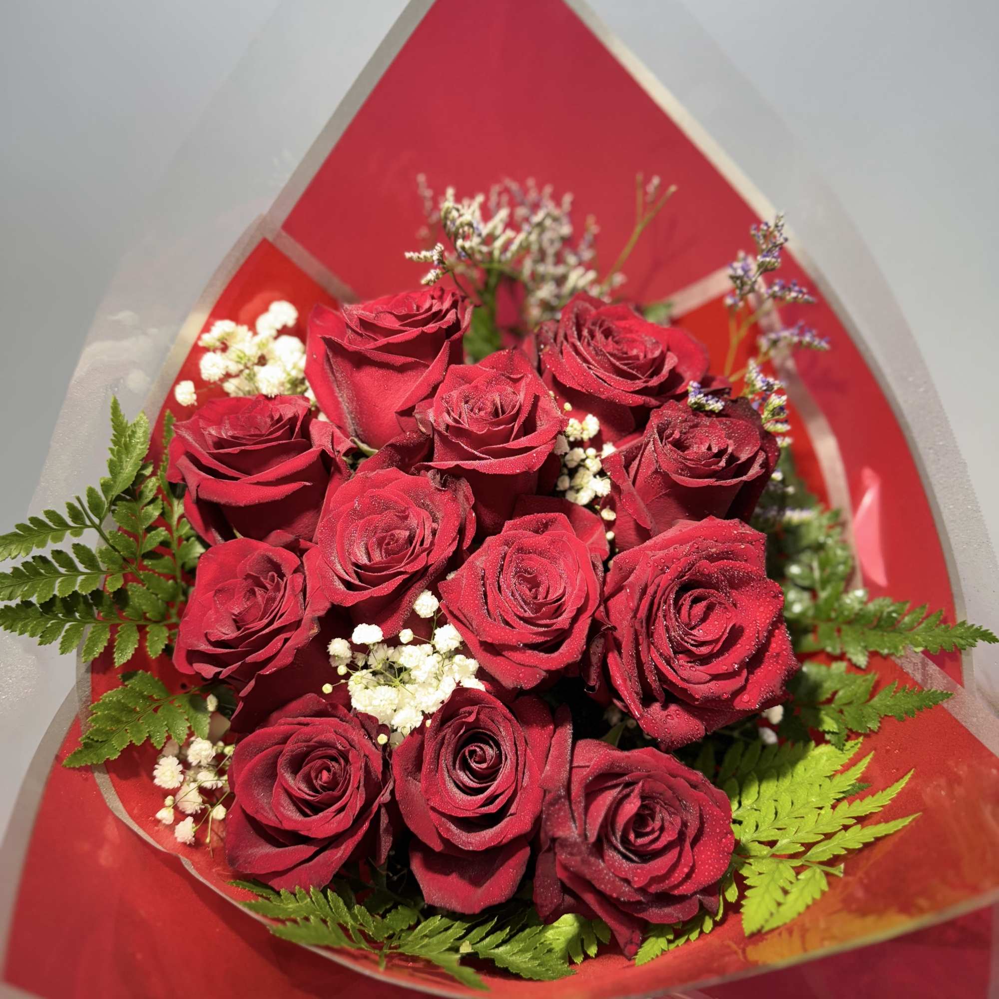 Twelve premium red roses arranged in elegant cellophane wrapping with lush green
