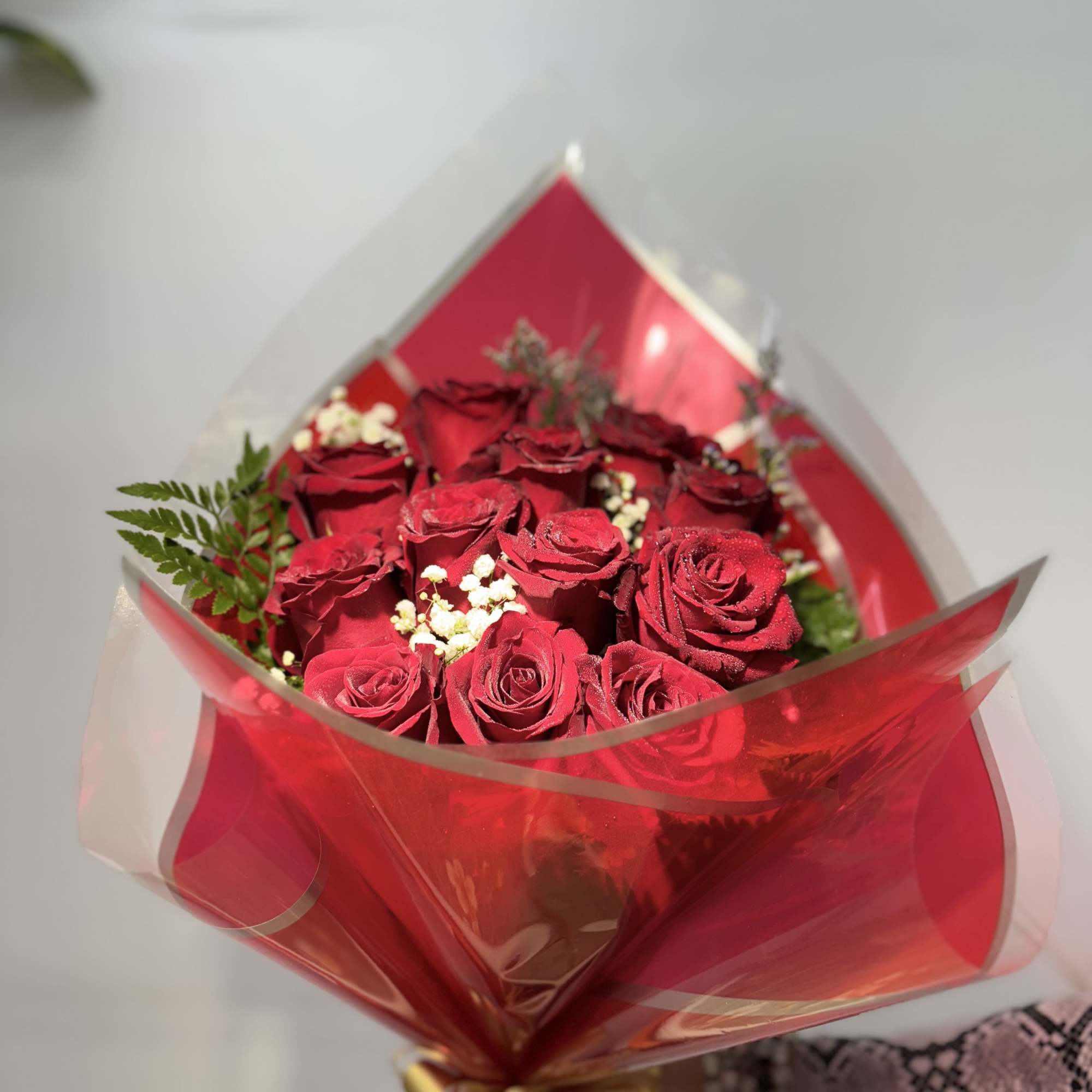 Twelve premium red roses arranged in elegant cellophane wrapping with lush green