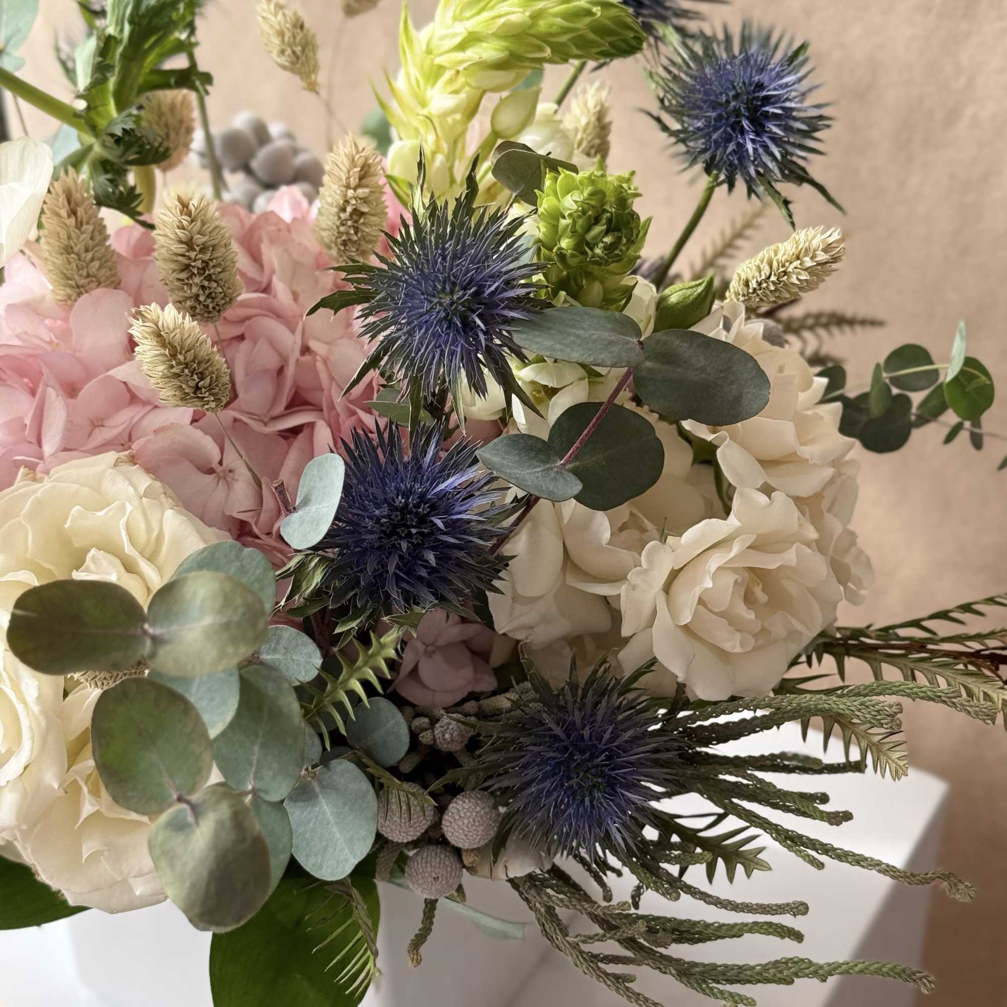 Pale pink and white flowers arranged in a white ceramic container. 