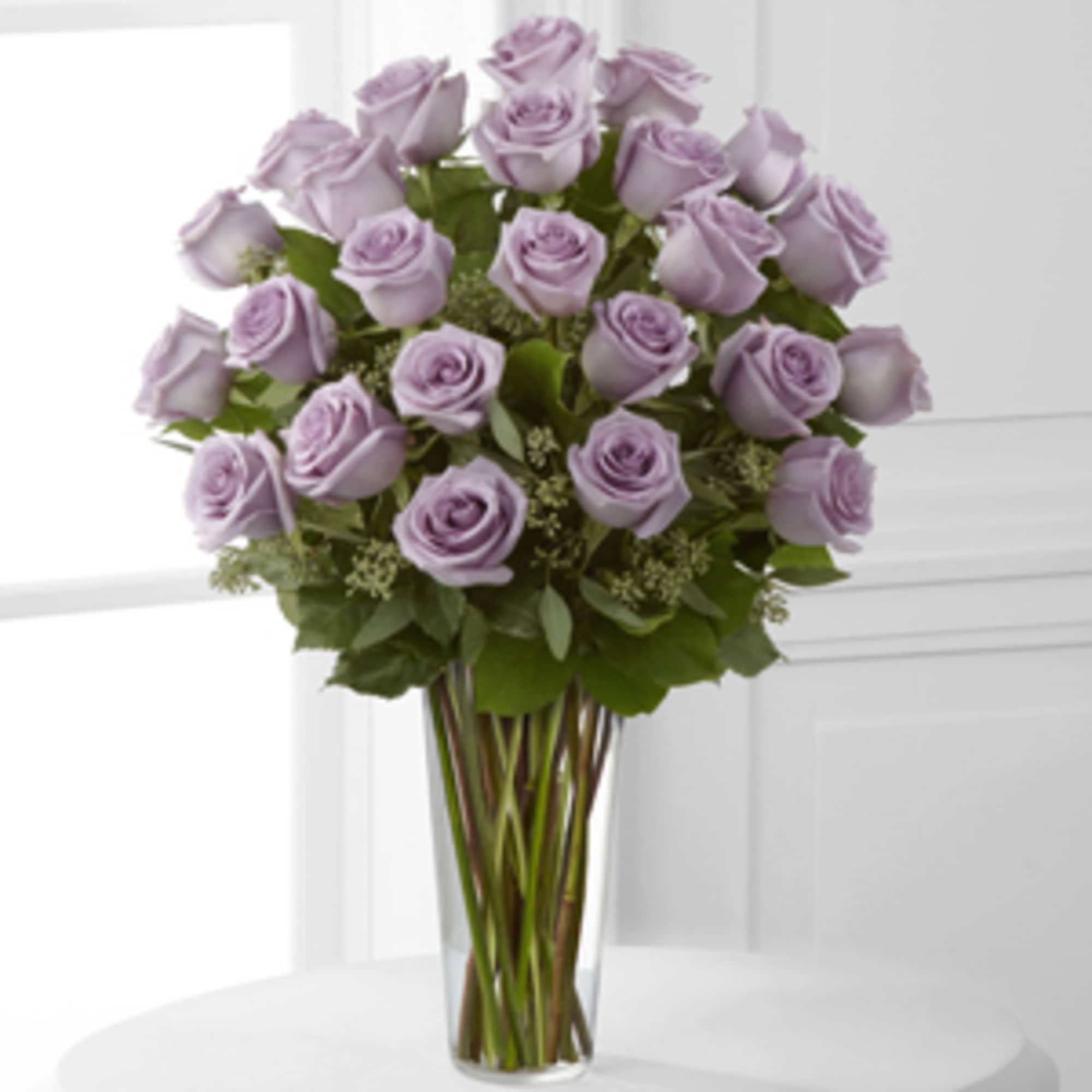 Lavender roses are designed a sparkling glass vase, accented with lush foliages.