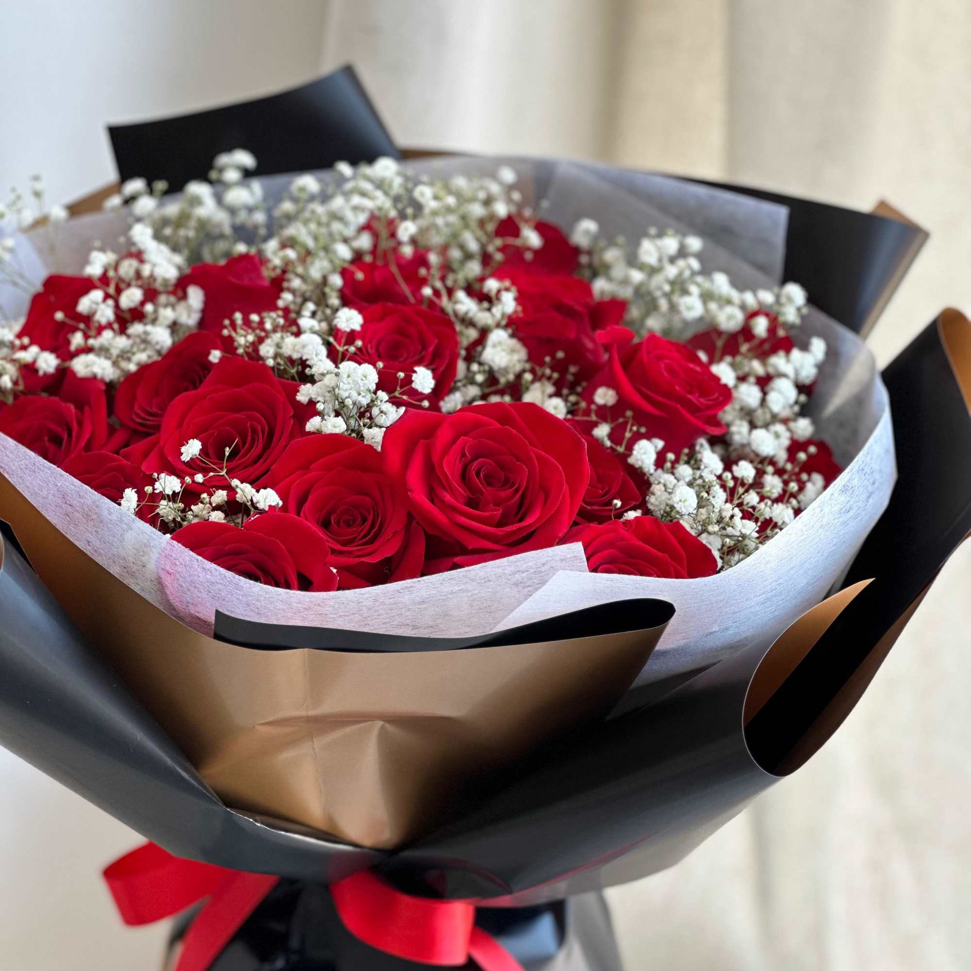 A round bouquet of roses and baby's breath, wrapped in black paper.