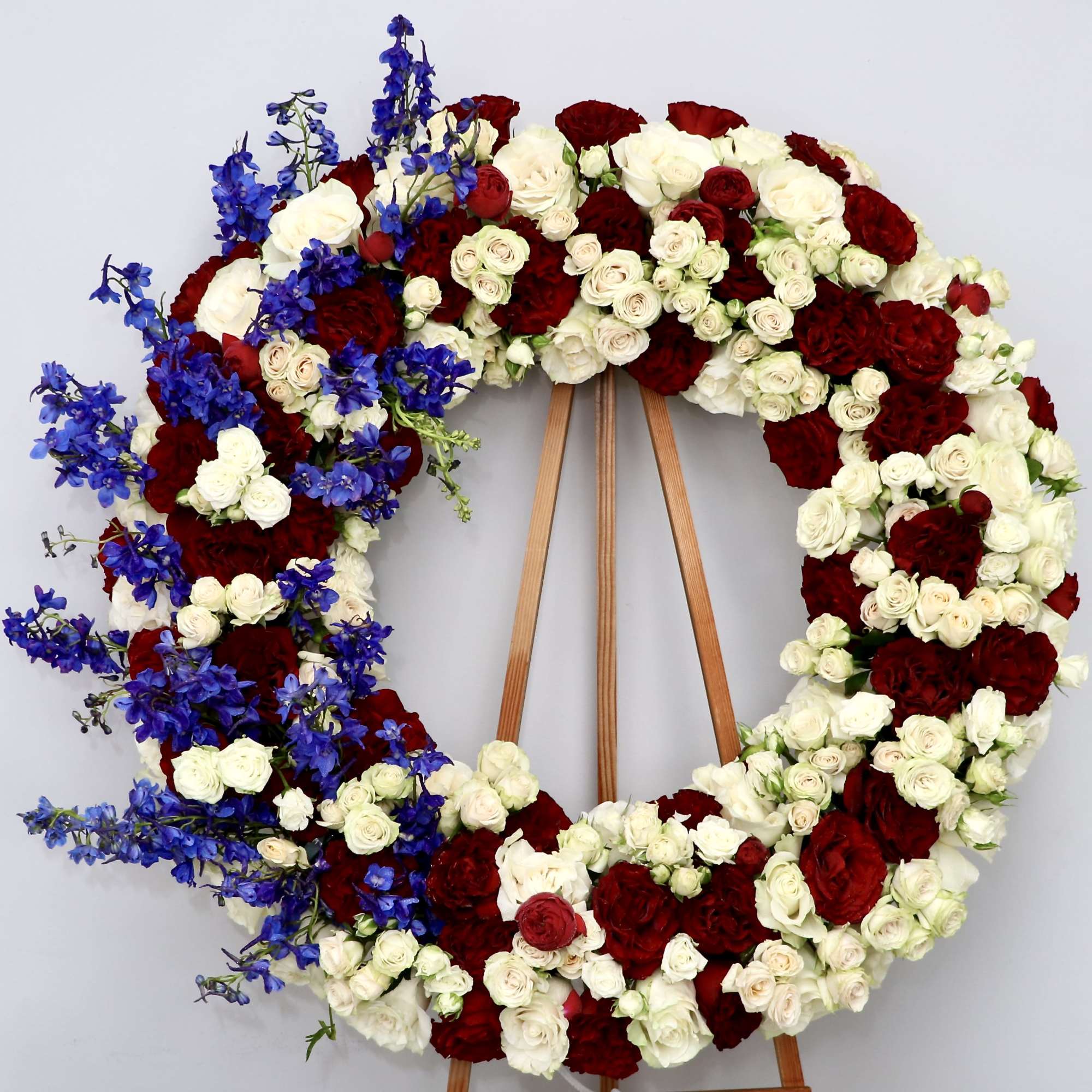 This wreath includes seasonal, reds, whites and blue flowers. 

We include easel