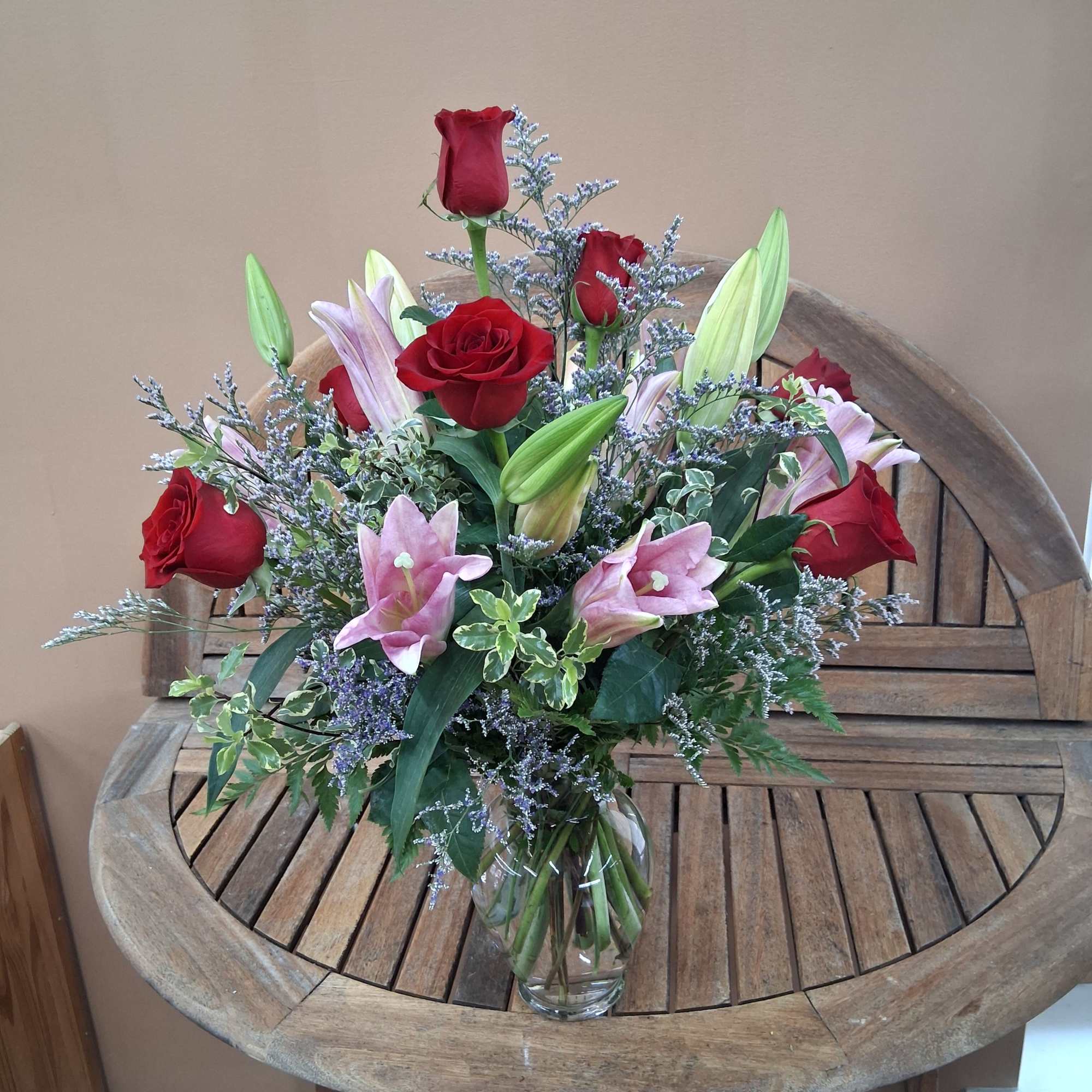 Red roses and pink lilies arranged in a vase with greens and