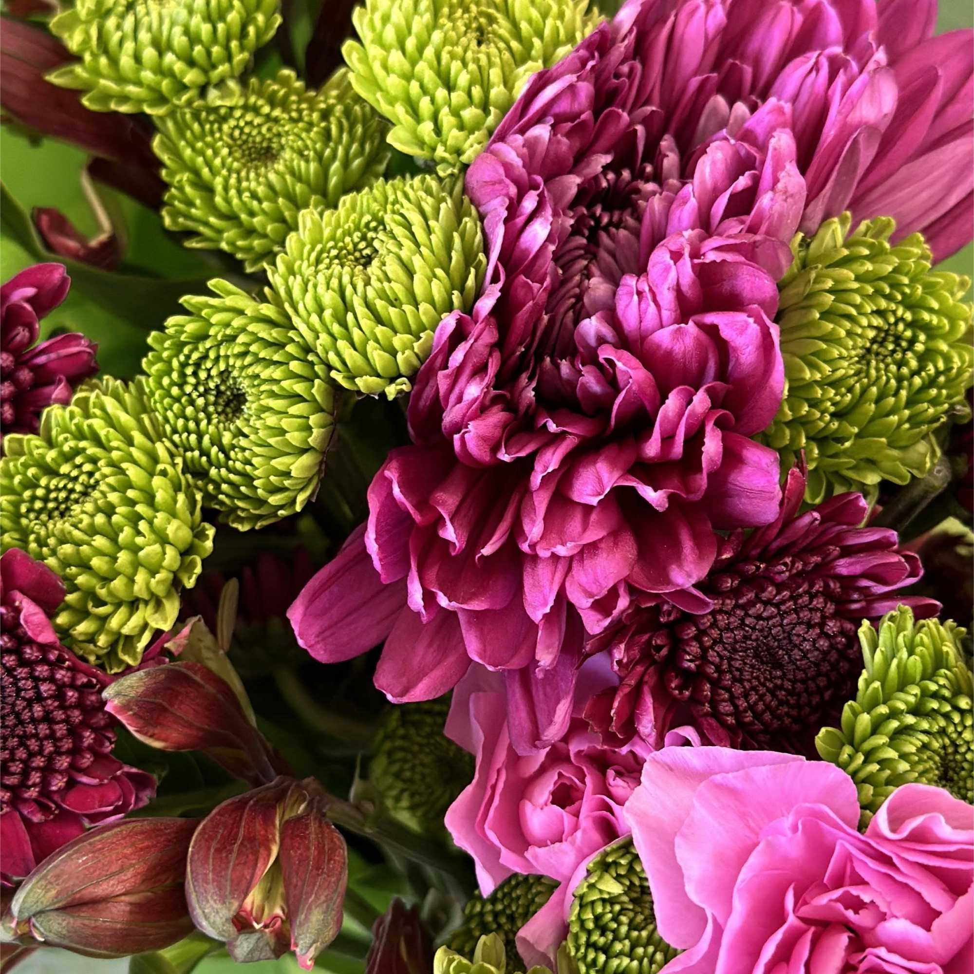 This bold and captivating arrangement of fuchsias, purples, and greens bursts with