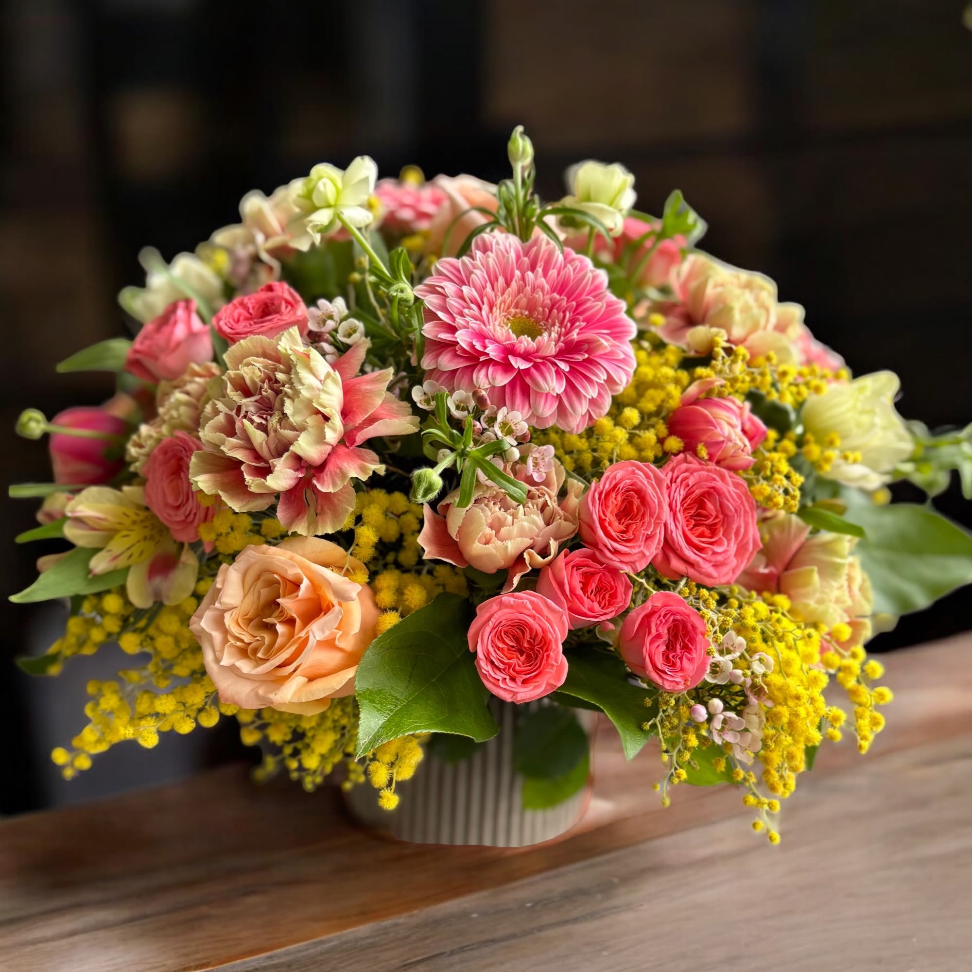 A seasonal arrangement of fragrant mimosa, coral spray roses and peach roses.