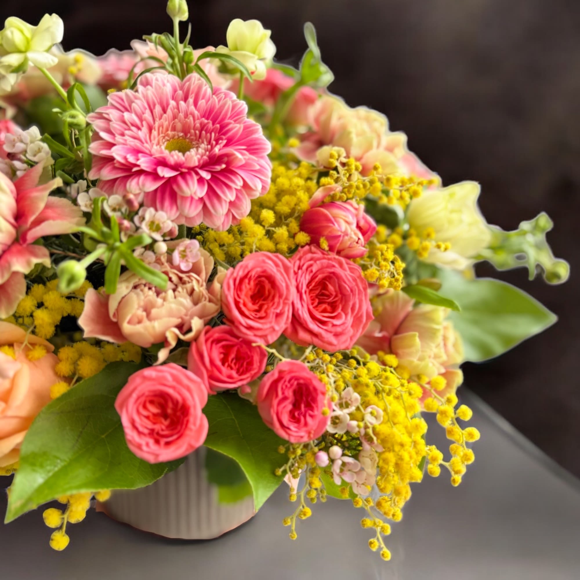 A seasonal arrangement of fragrant mimosa, coral spray roses and peach roses.