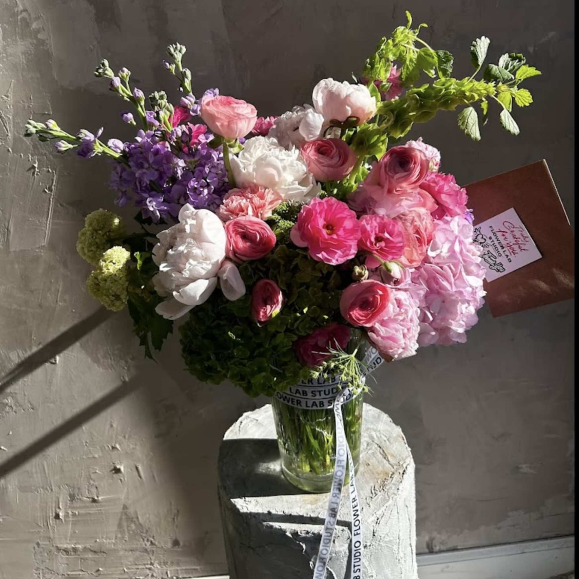 Featuring delicate peonies, ranunculus, soft hydrangea, and romantic roses, this arrangement is