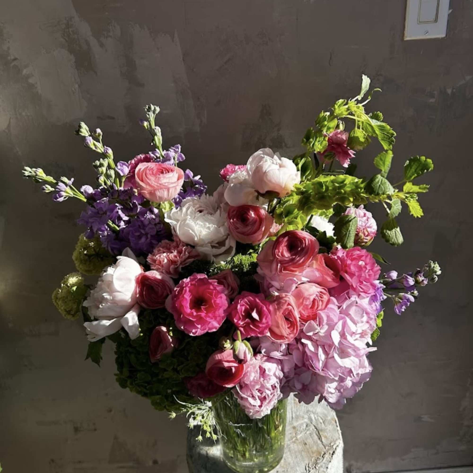 Featuring delicate peonies, ranunculus, soft hydrangea, and romantic roses, this arrangement is