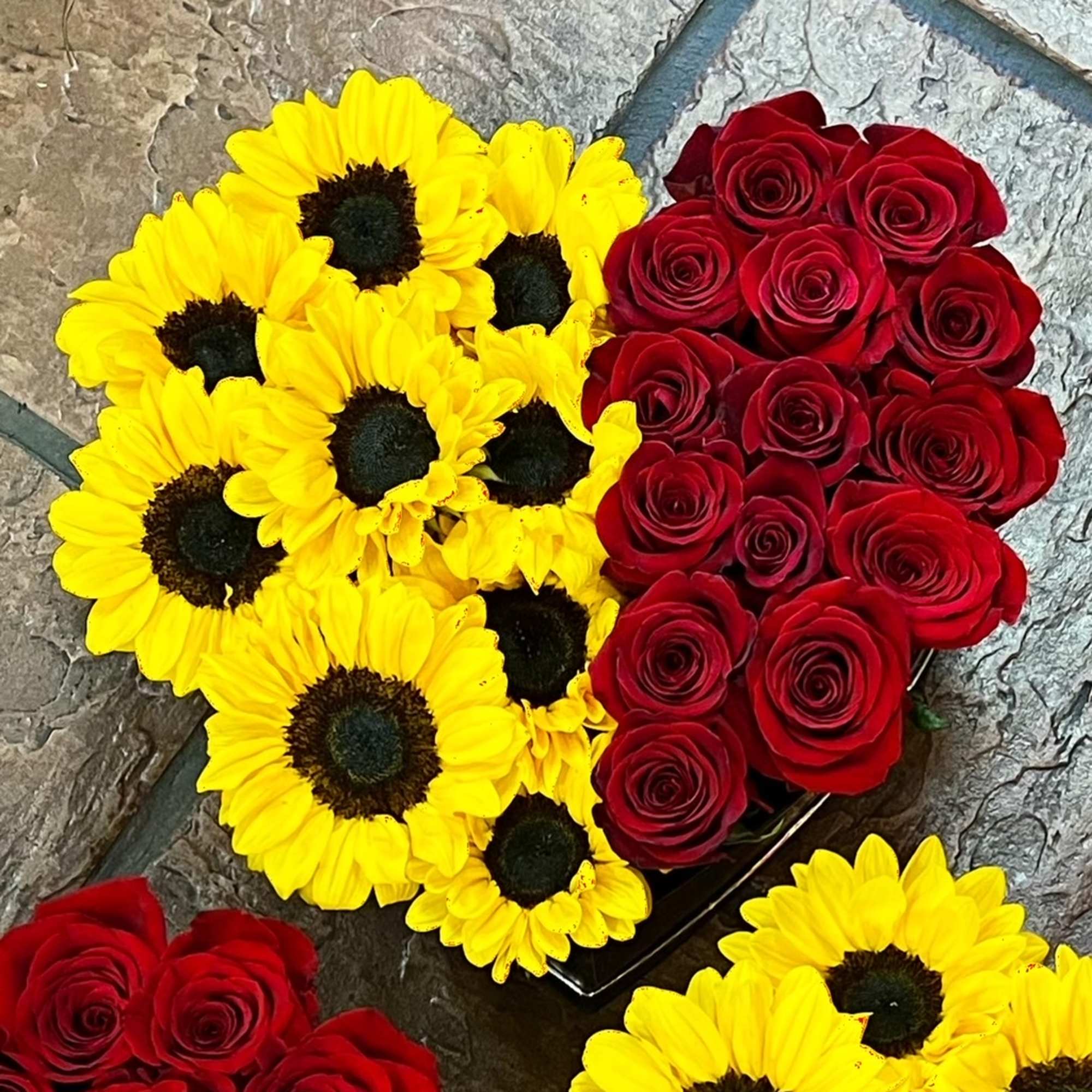 Red roses and sunflowers are arranged in a heart box