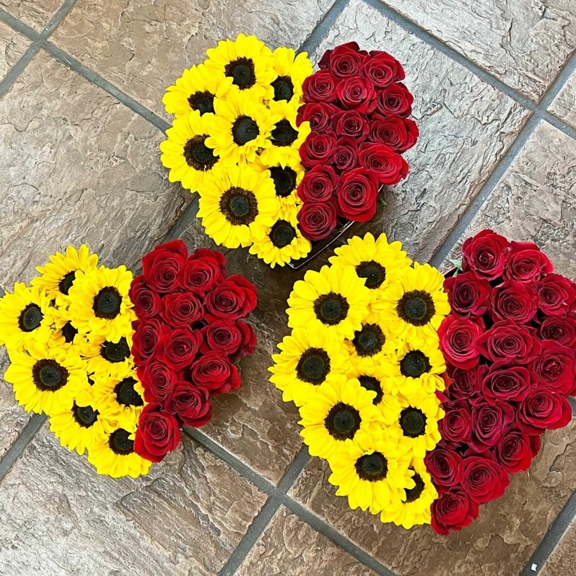 Red roses and sunflowers are arranged in a heart box