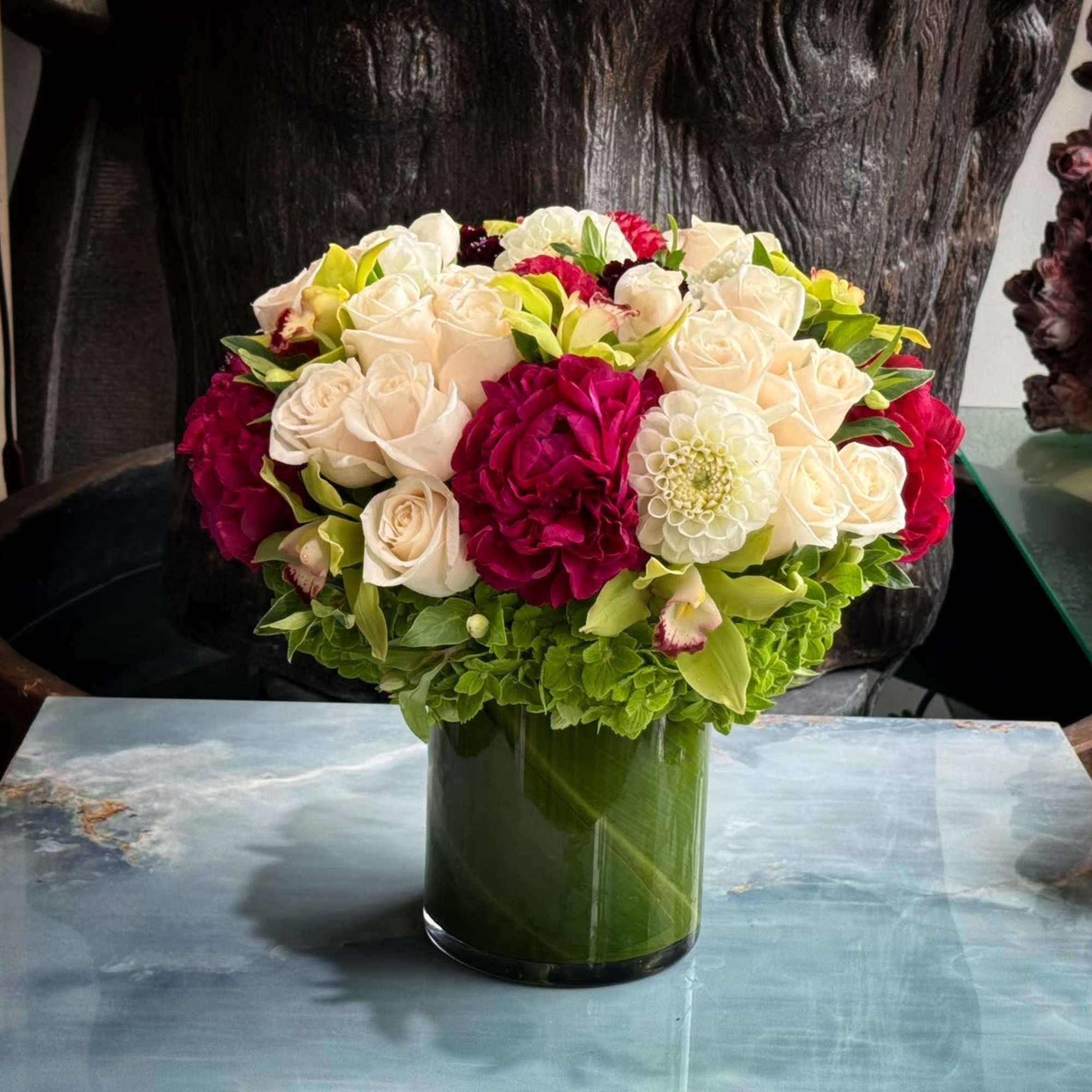 Green Cymbidium Orchids, Roses and Coffee Beans in circular glass vase.