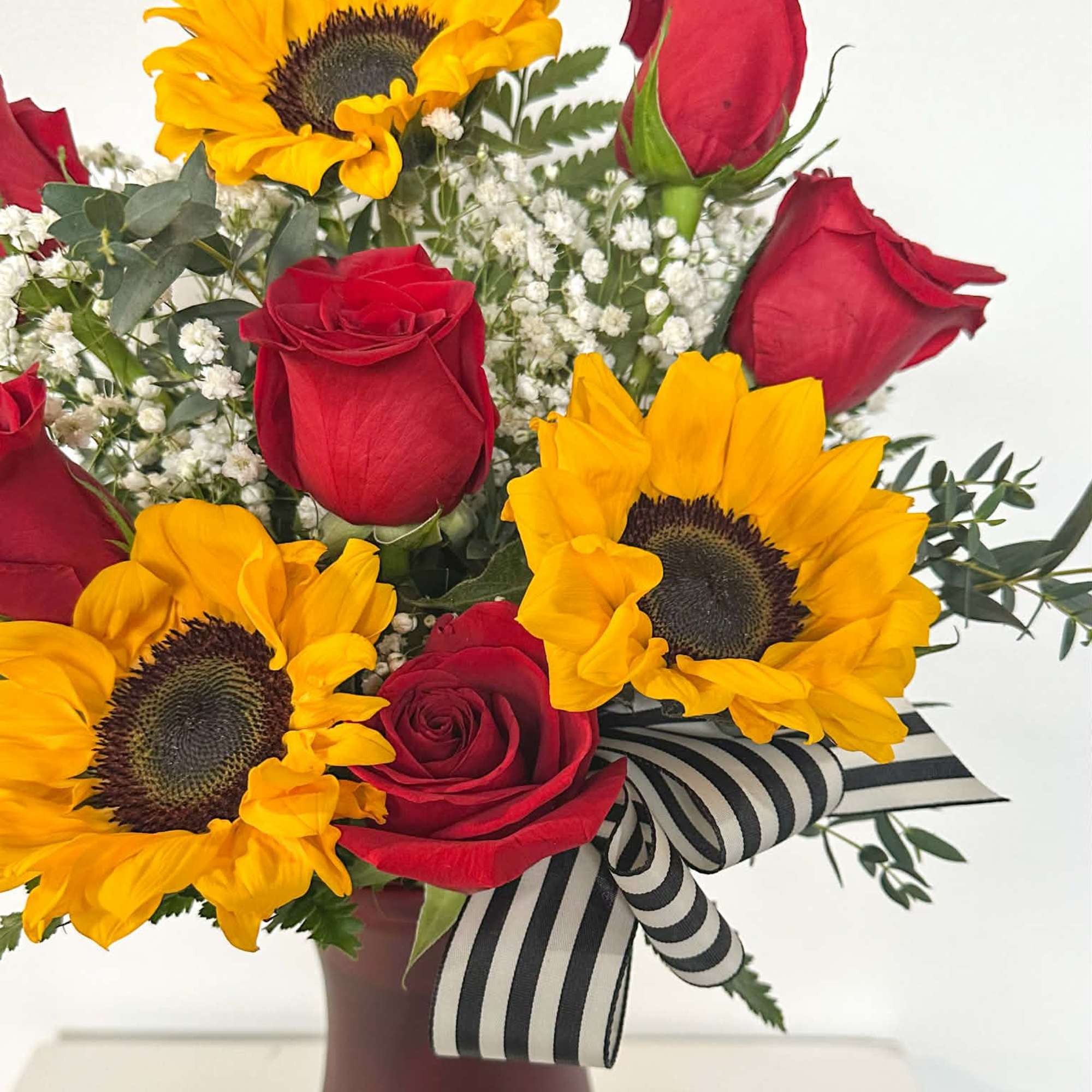 Sunlit Romance pairs vibrant sunflowers with classic red roses, soft white accents