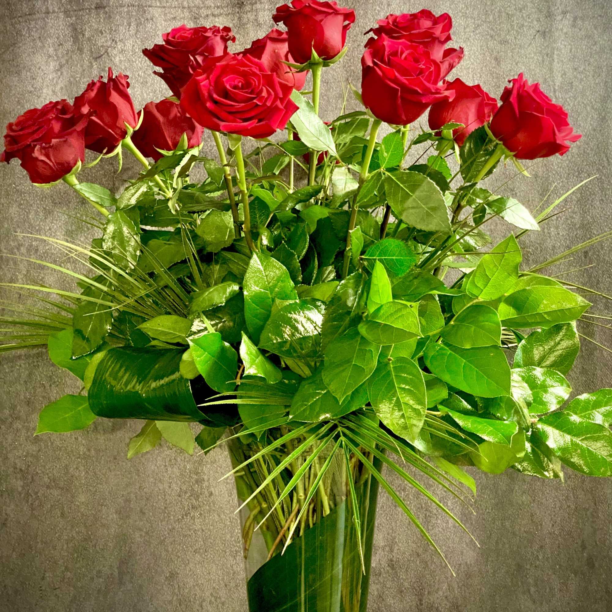 One Dozen Premium Long Stem Red Roses arranged with tropical foliage in