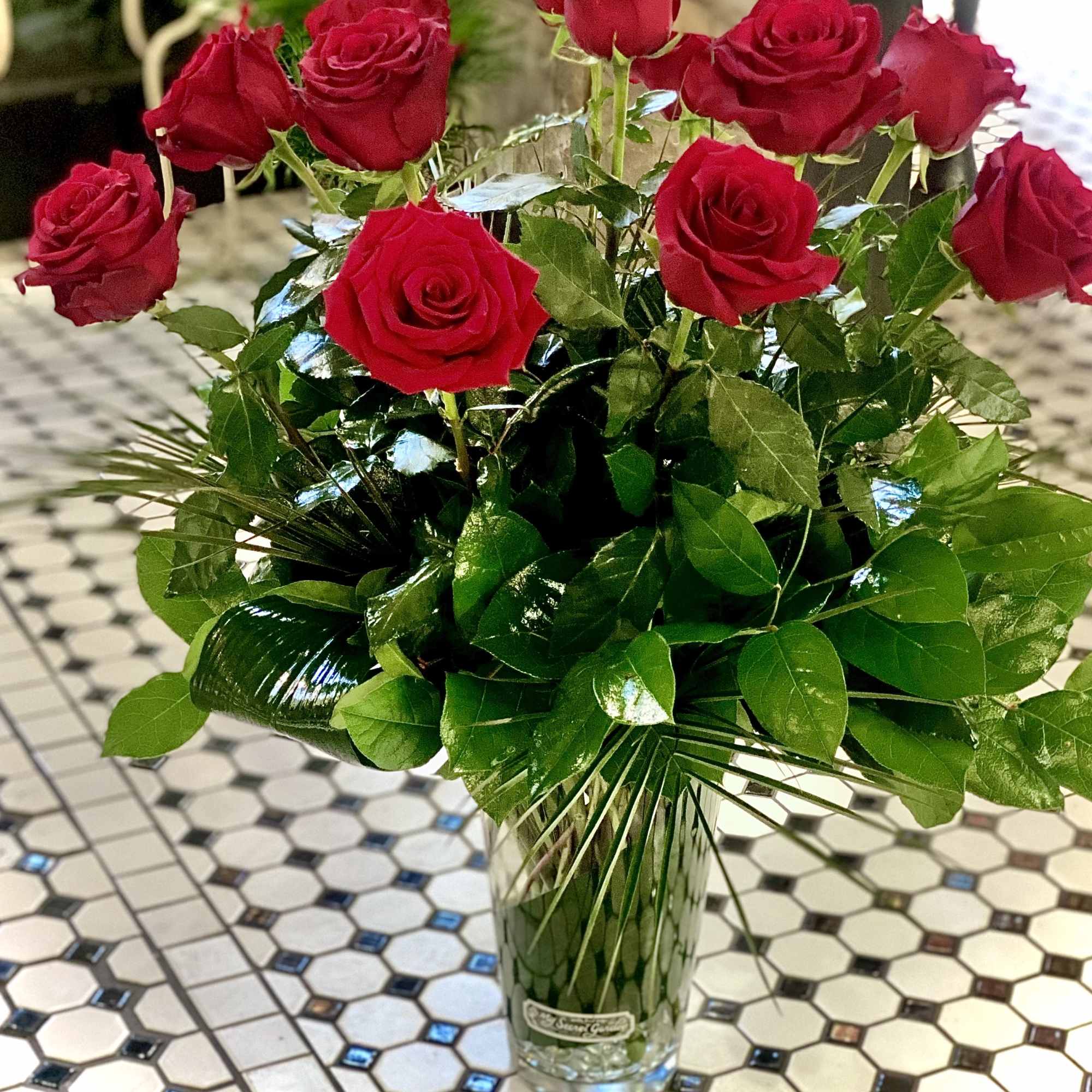 One Dozen Premium Long Stem Red Roses arranged with tropical foliage in