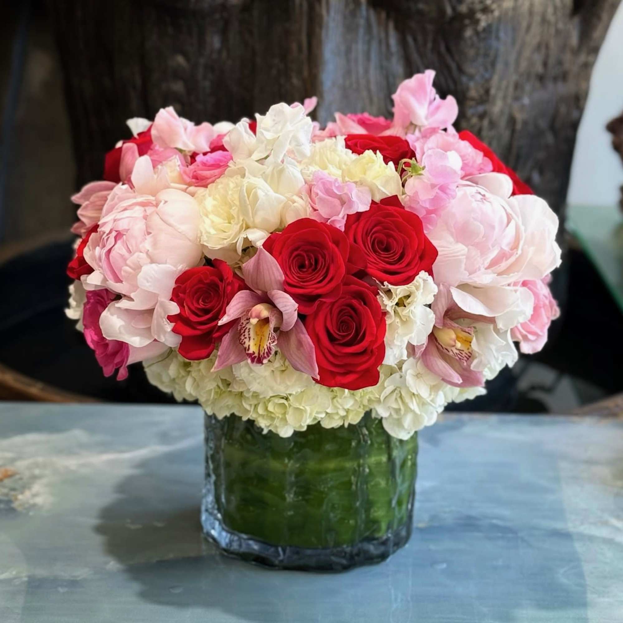 Roses, Hydrangeas, and Cymbidium Orchids in a ceramic vase. 