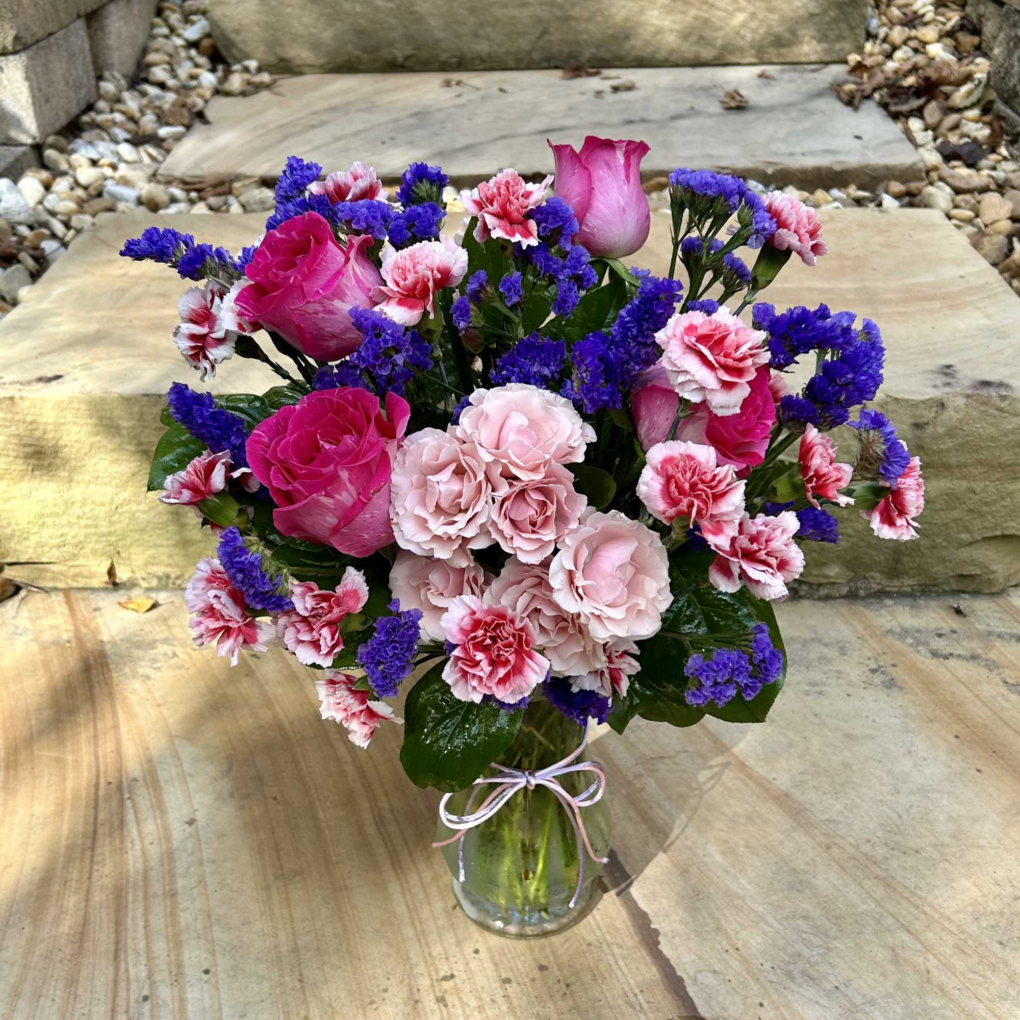 A pink and purple arrangement of roses, mini carnations, spray roses and