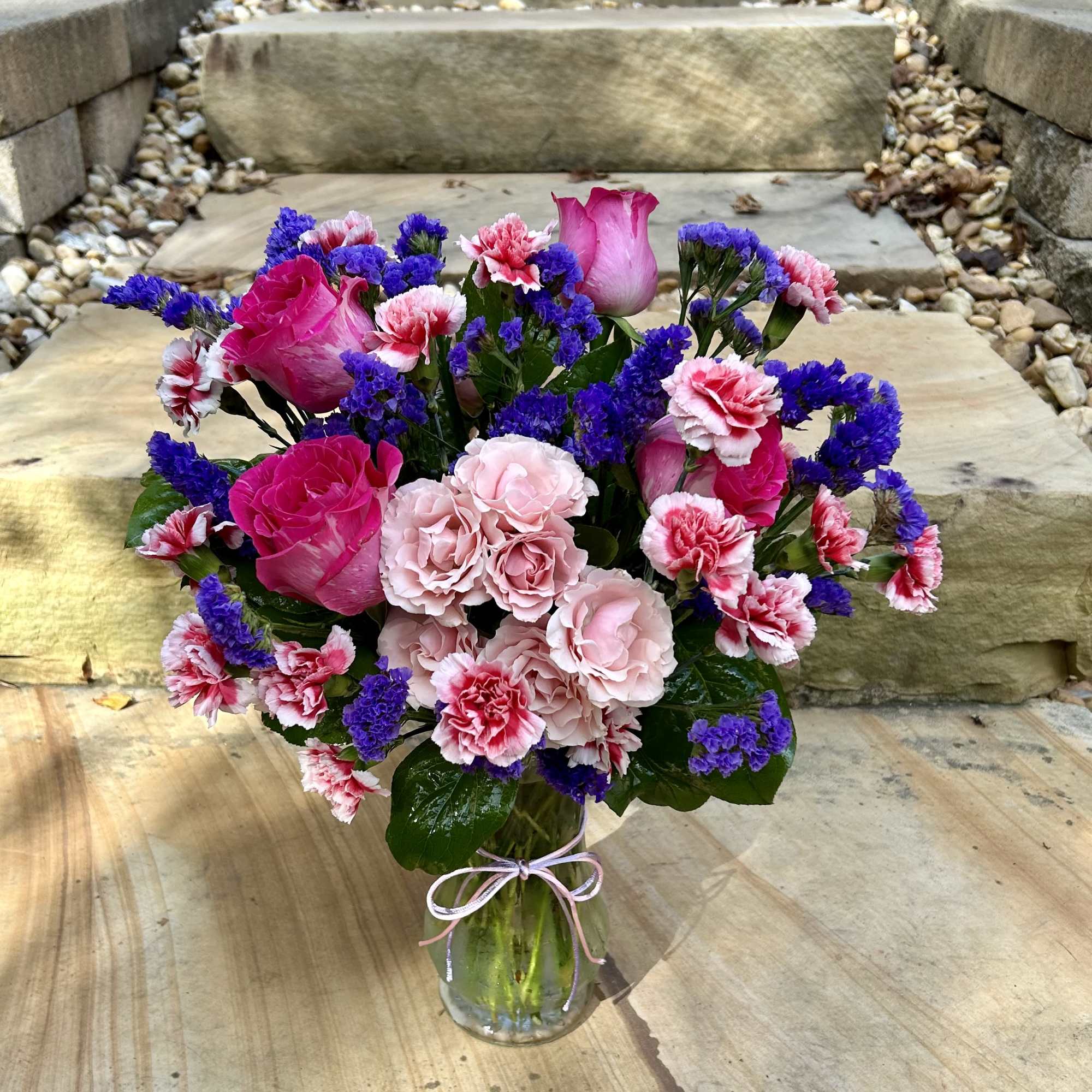 A pink and purple arrangement of roses, mini carnations, spray roses and